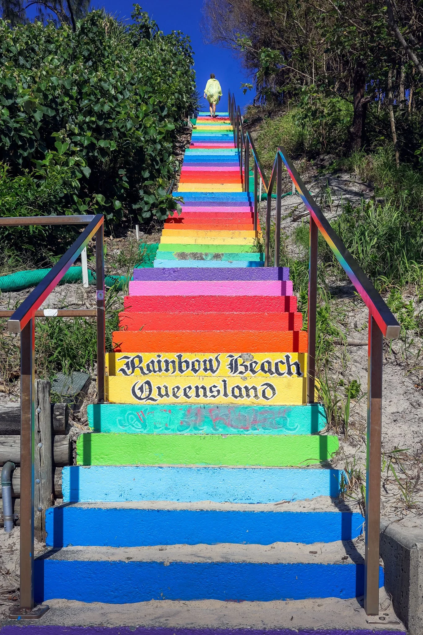 A solitary figure stands atop the iconic rainbow-colored steps at Rainbow Beach, Queensland.