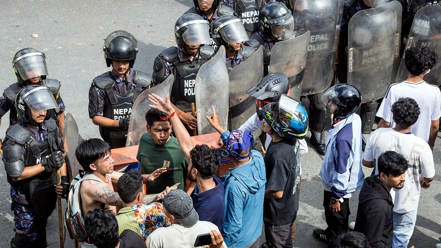 [Act I: Assembly]. A protester intervenes as tensions flare between angry demonstrators and police.