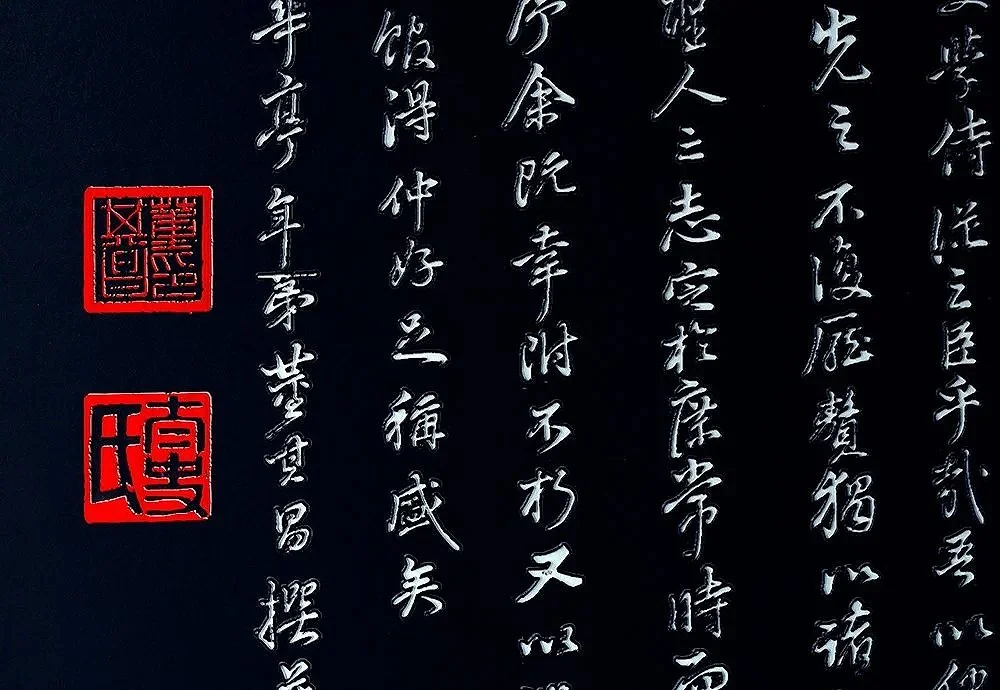 Close-up of Chinese calligraphy on a black background with two red kanji seal stamps.
