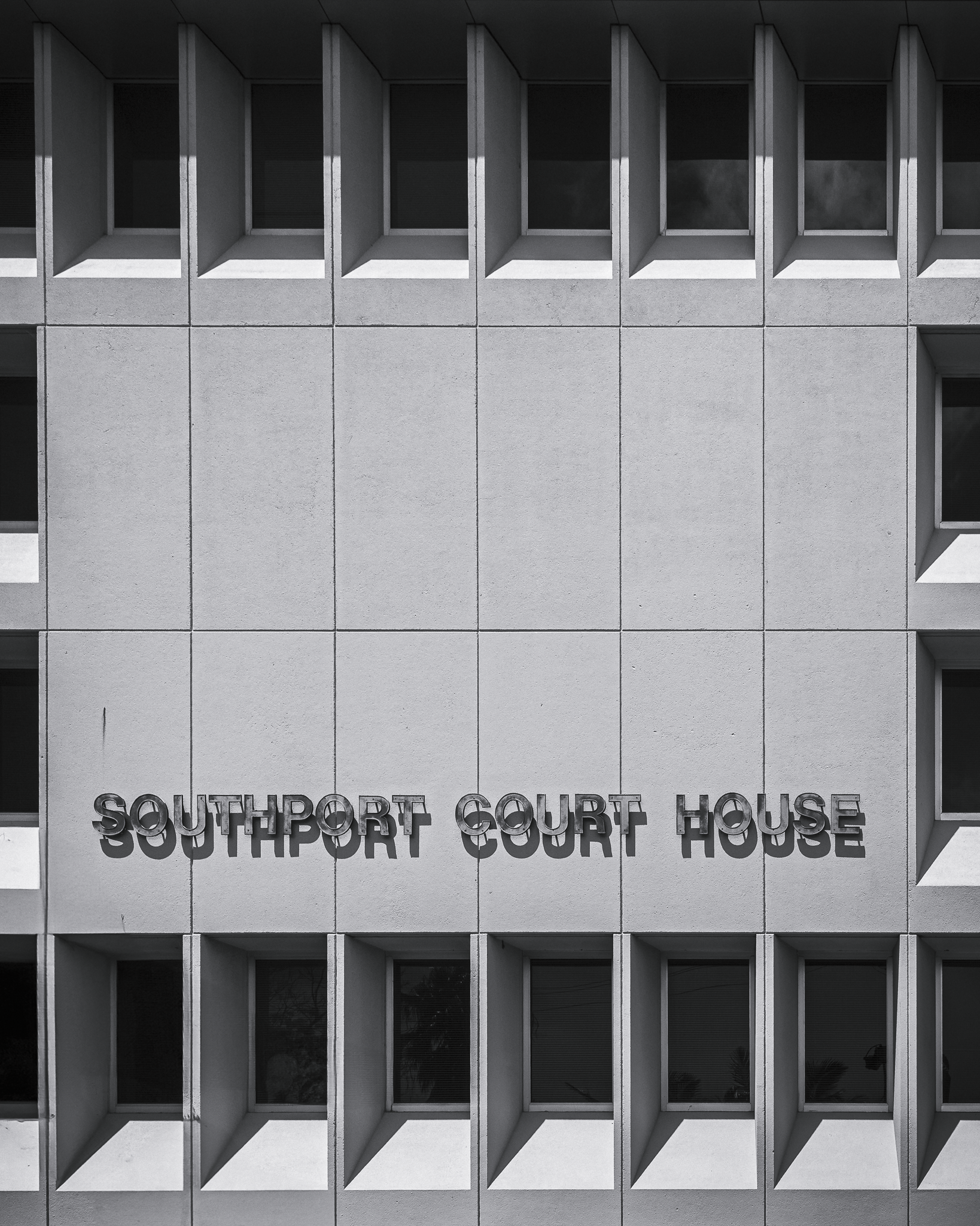 Sunlight strikes the "Southport Court House" lettering on the building facade, creating an overlapping double exposure effect that blurs the text in an artistic interplay of light and shadow.