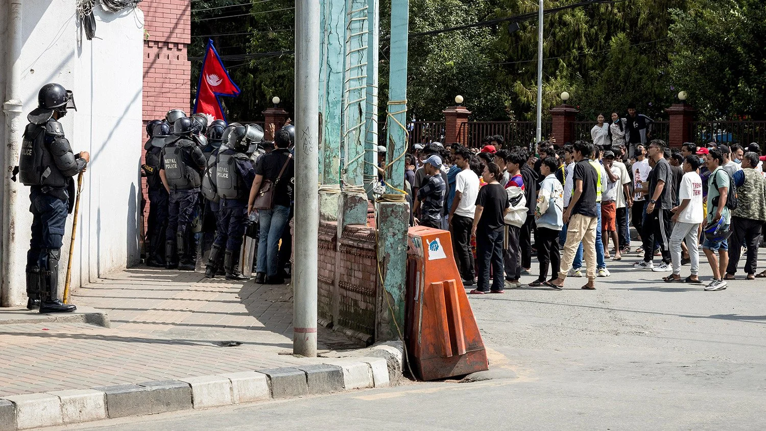 [Act II: Collision]. A protester is watched by a police officer near Durbar Square.