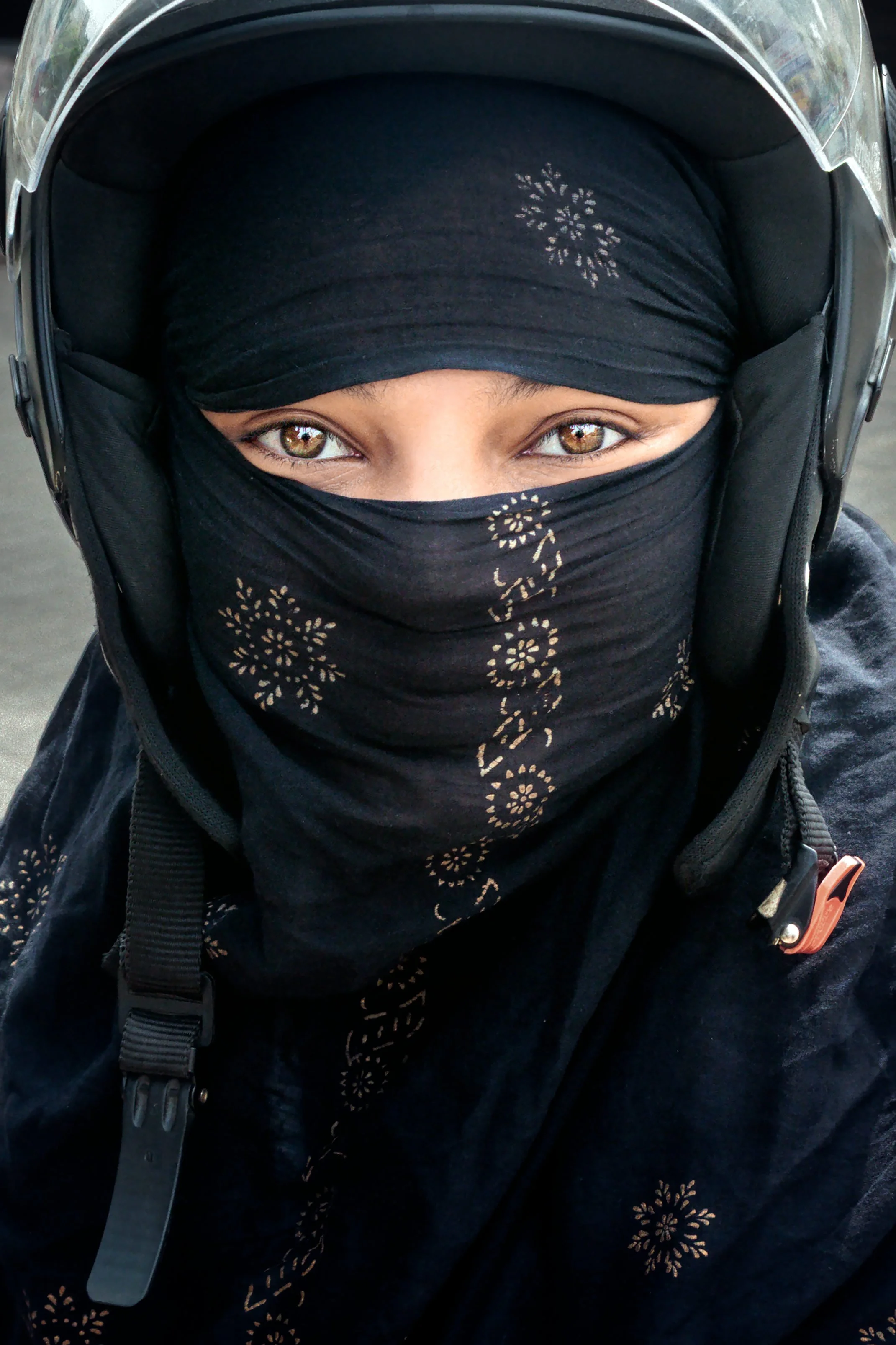 A woman rides her motorbike through the streets, wearing both a protective helmet and niqab, embodying the intersection of modern mobility and traditional dress.