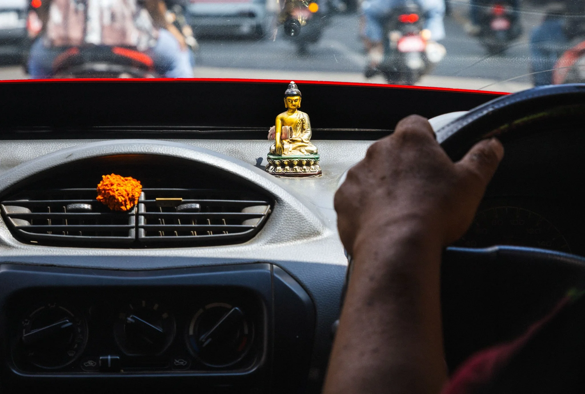 A small Buddha statue clutches 200 rupee notes inside a Nepalese taxi, creating an ironic juxtaposition with Buddhism's teachings on non-attachment to material wealth.