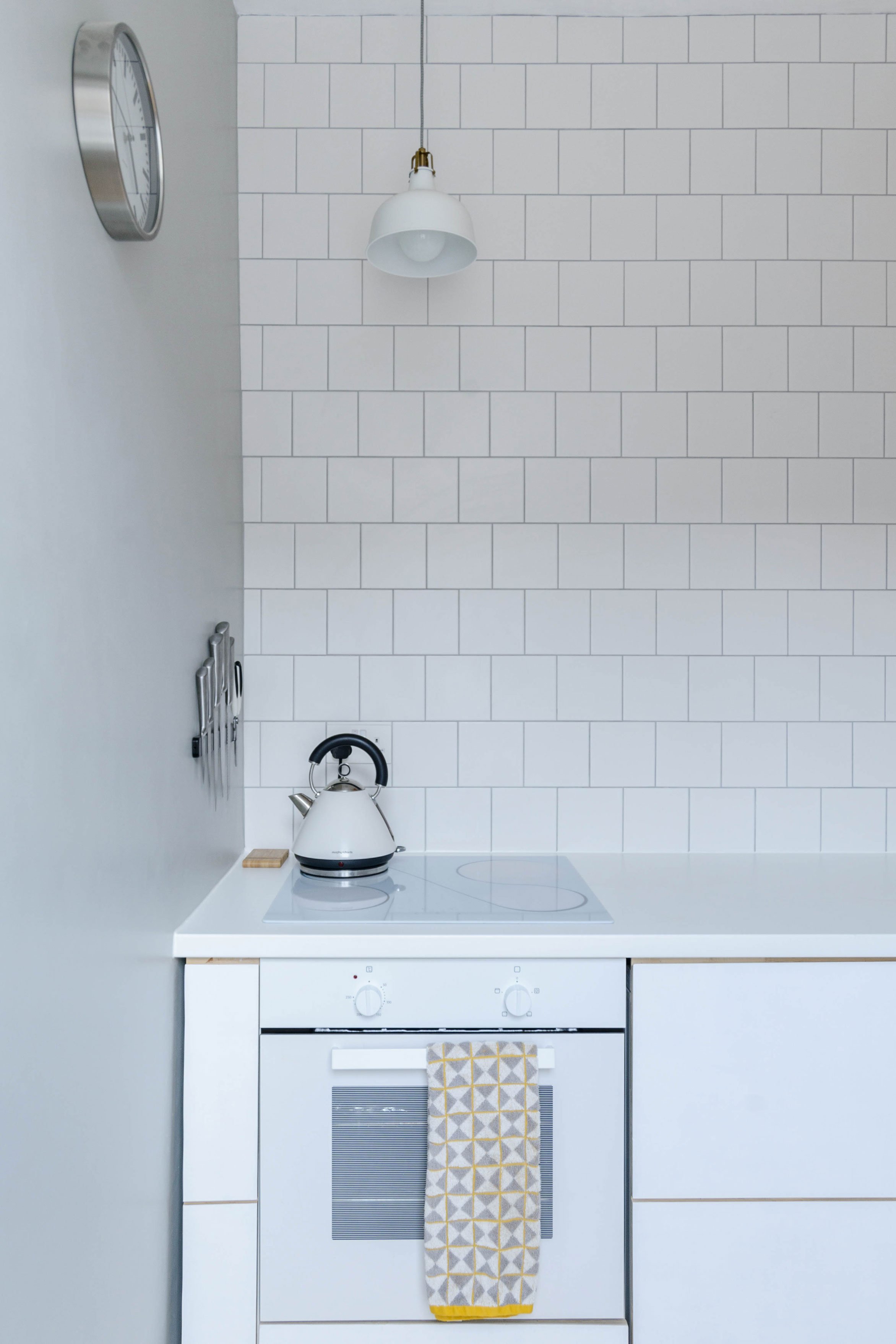 Modern interior architecture of a kitchen space with white cabinets and a white tiled wall.