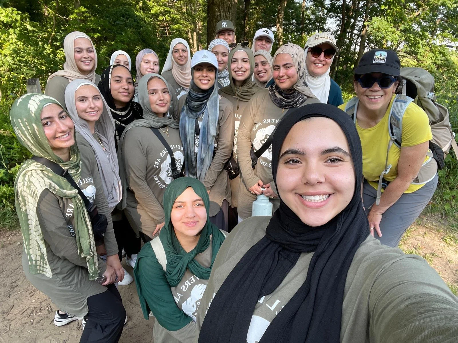 A group of teenage Muslim girls in matching camp t-shirts pose for a selfie while hiking with SUM's Mary Daniels