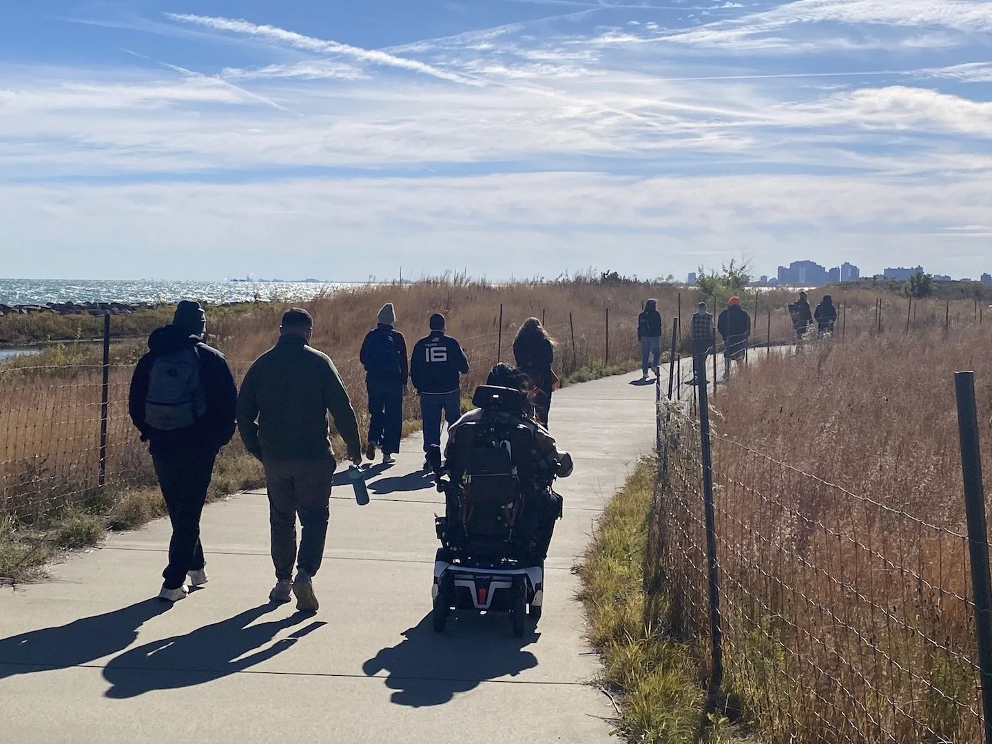 A group of people walk and use a wheelchair on a prairie path