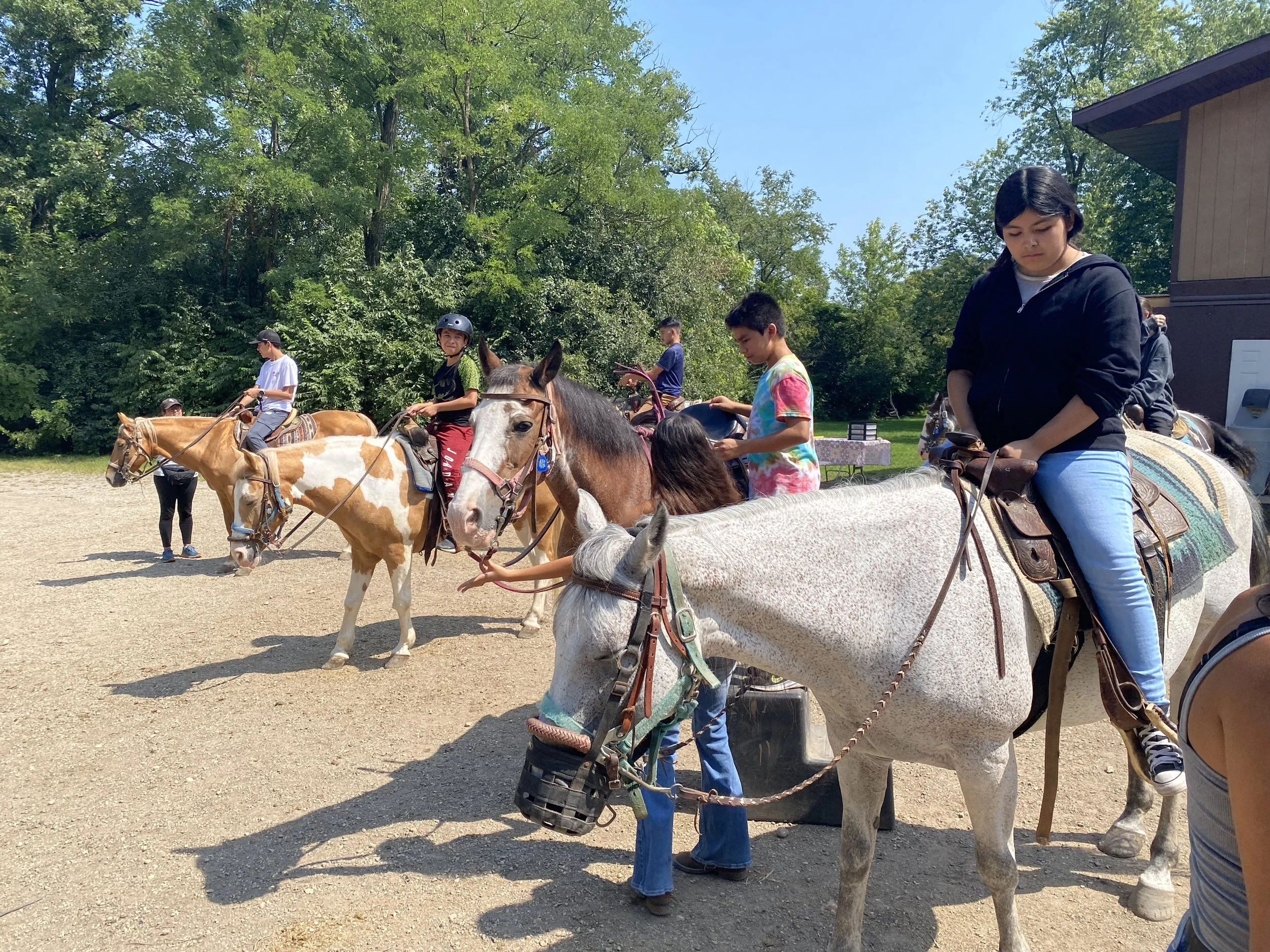 Multiple kids mount horses in front of a barn