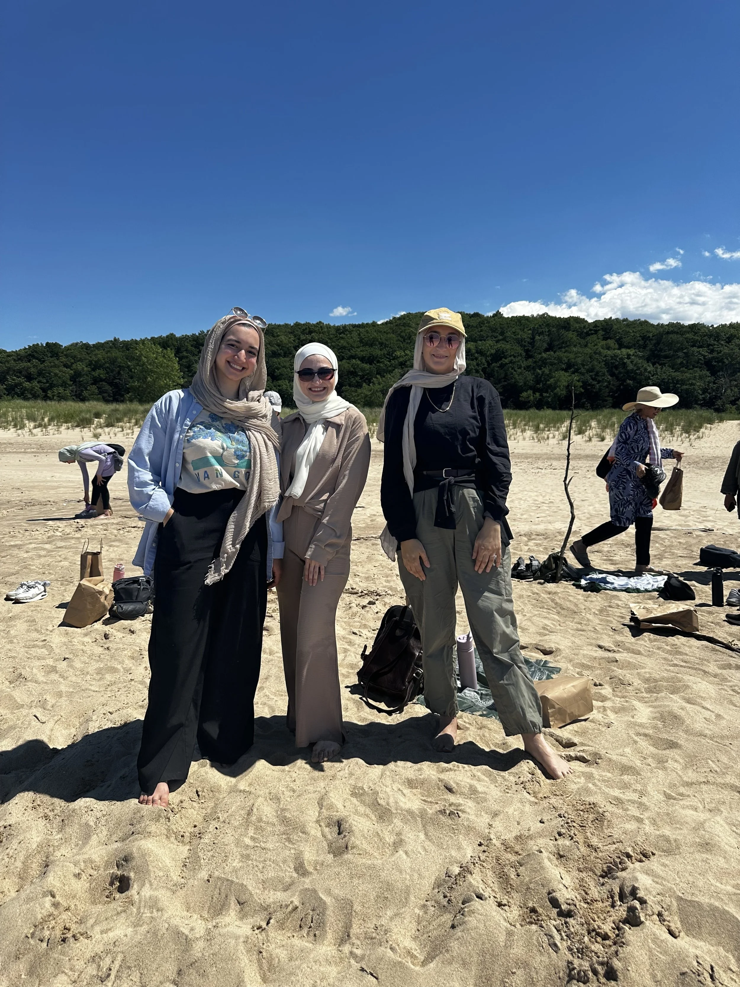 three women standing together posing for their picture on the sandy beach