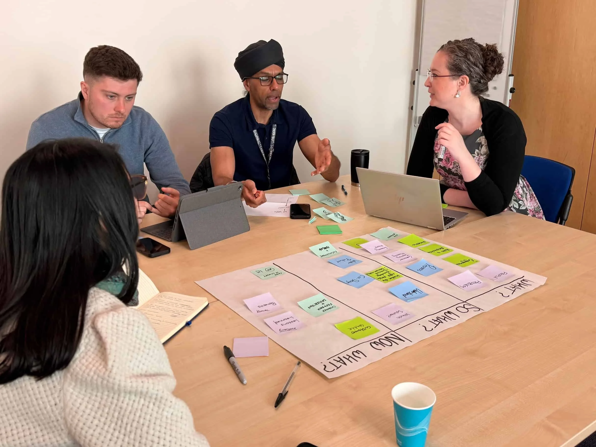 Four people sat at a desk actively discussing something. There is a worksheet on the desk.
