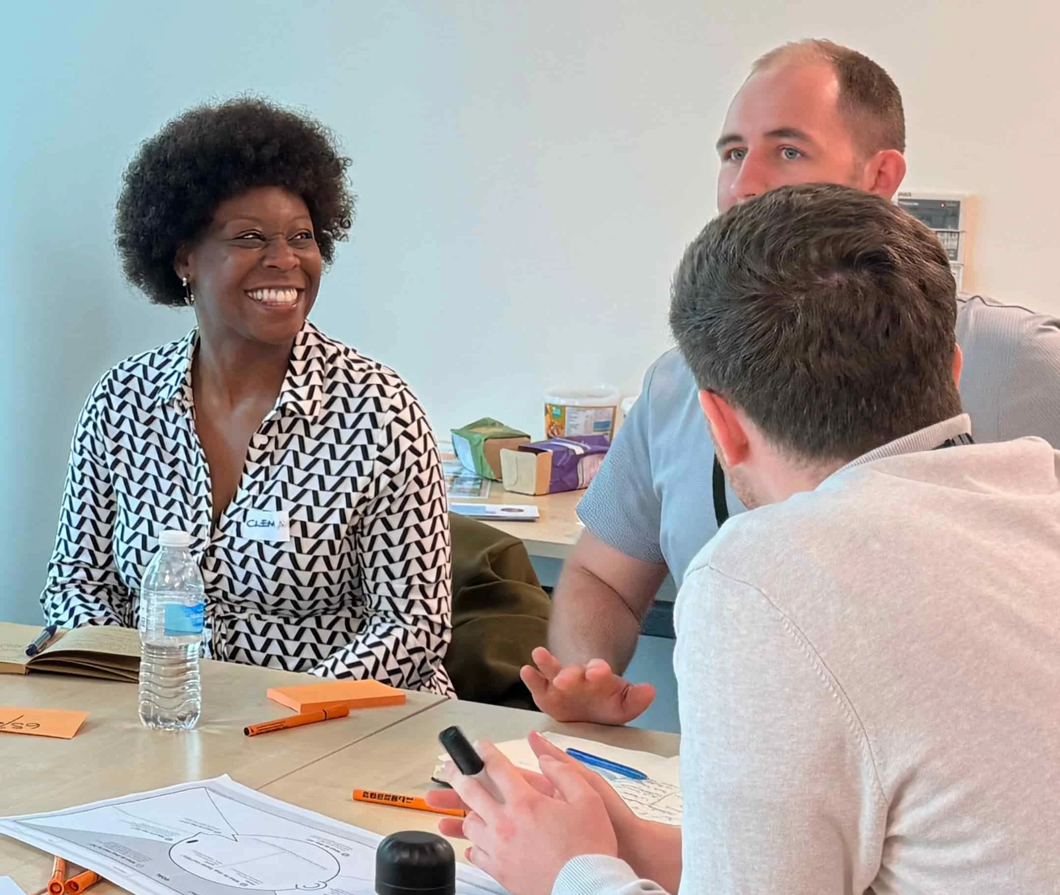 Three people sat at a desk engaged in conversation. They have a worksheet on the desk. They are smiling.