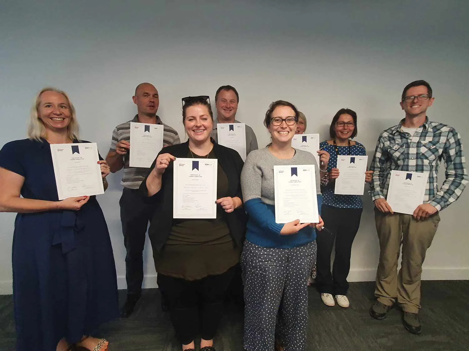 Three men and four women hold up certificates showing they have completed Service Works' Service Design in Practice programme.