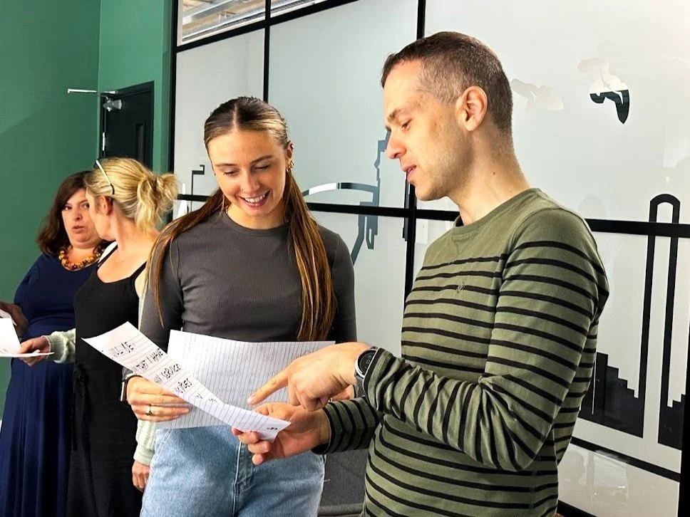A white man and woman stood together looking at a piece of paper. The man is pointing at the paper. They look engaged and happy.