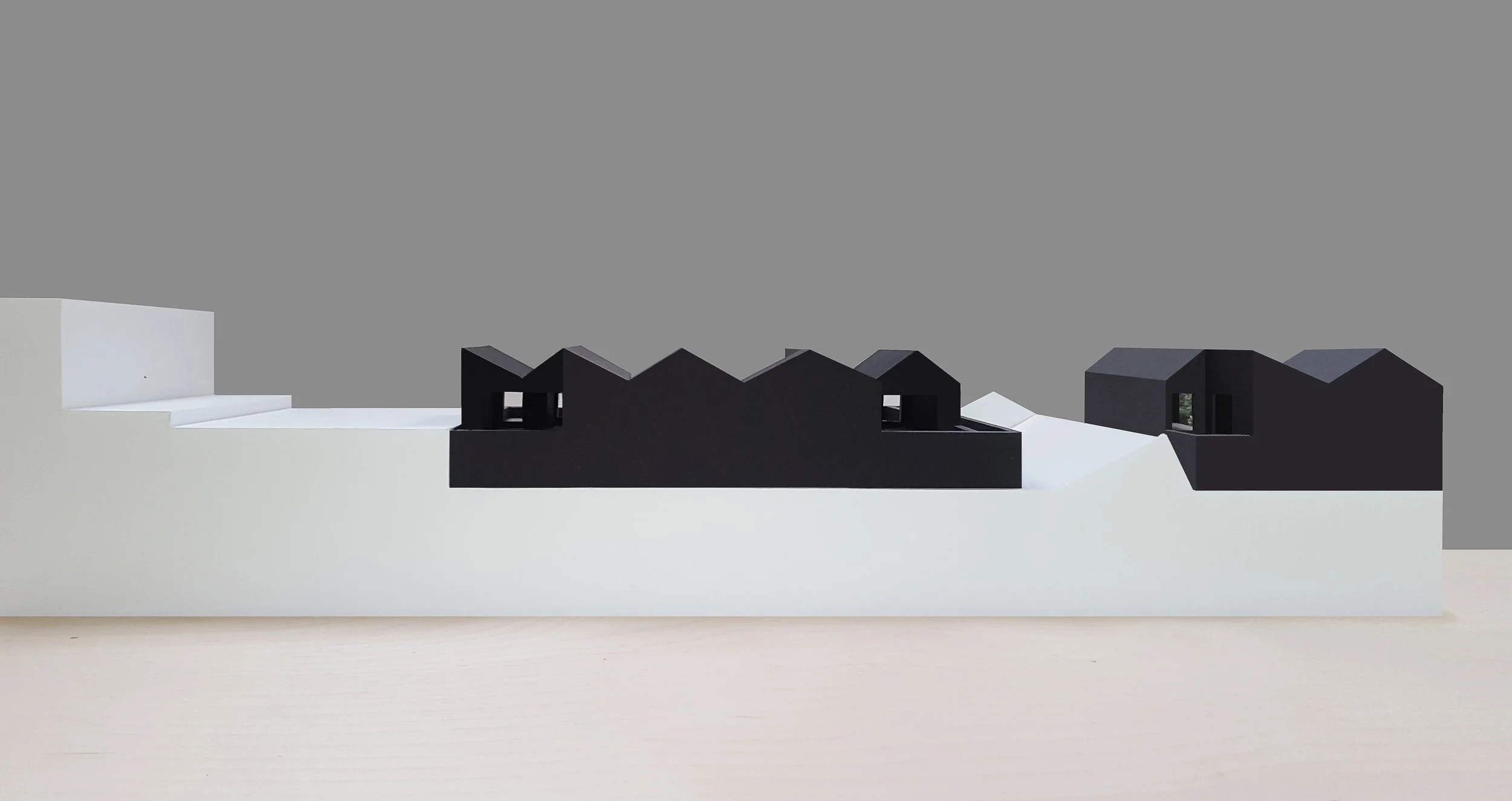 Architectural scale models of modern houses, black and white, placed on a white platform against a gray background.