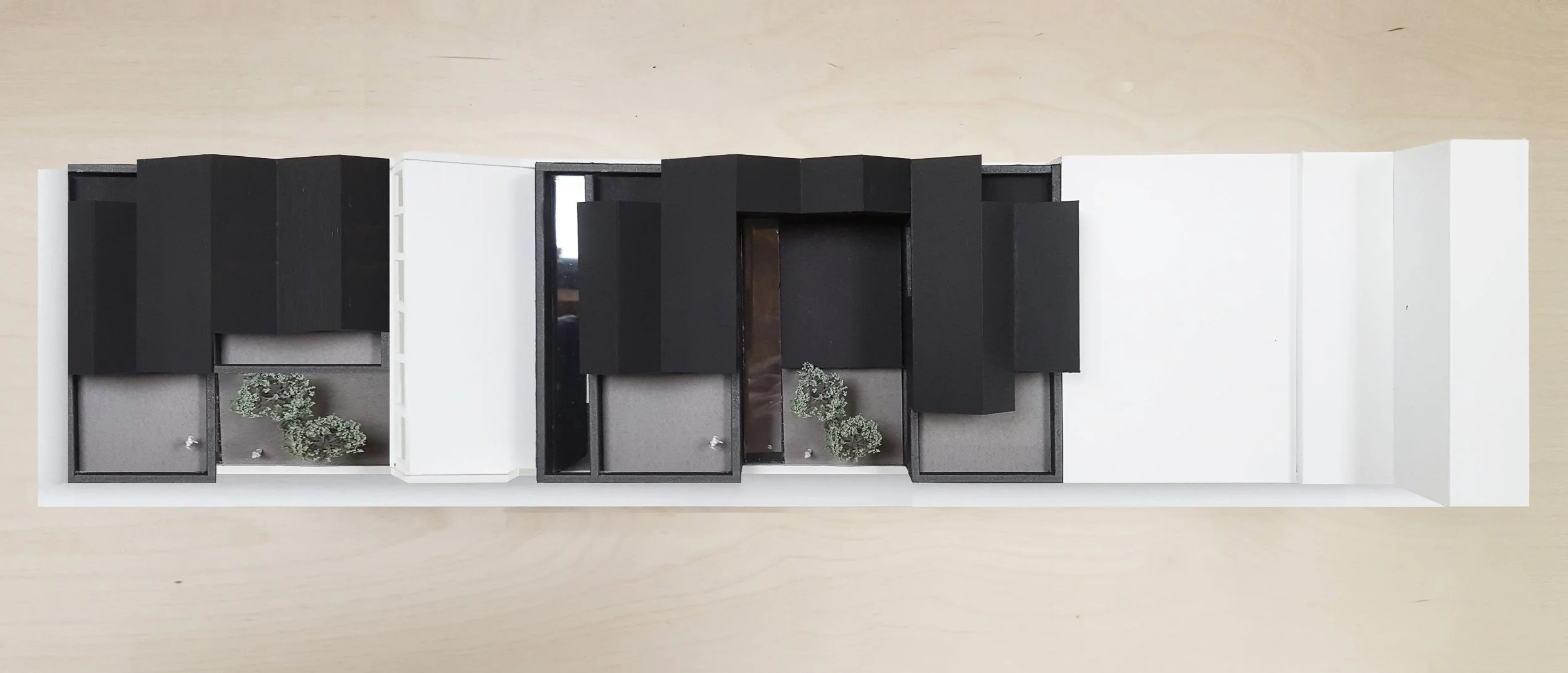 Top view of a modern architectural model with black, white, and gray structures and small greenery elements.