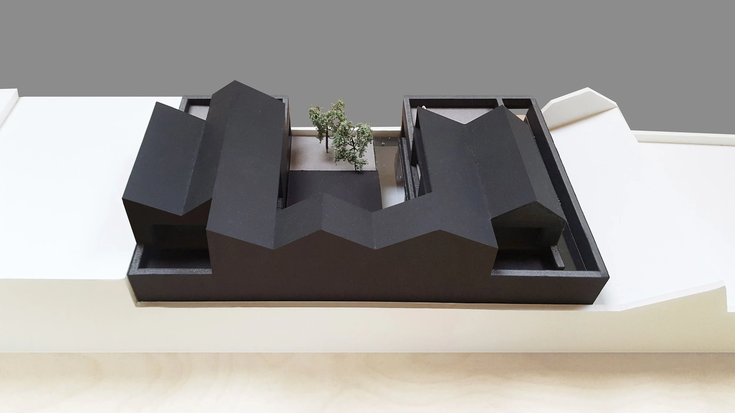 Architectural model of a modern building with black angular roof sections and small trees in the courtyard.