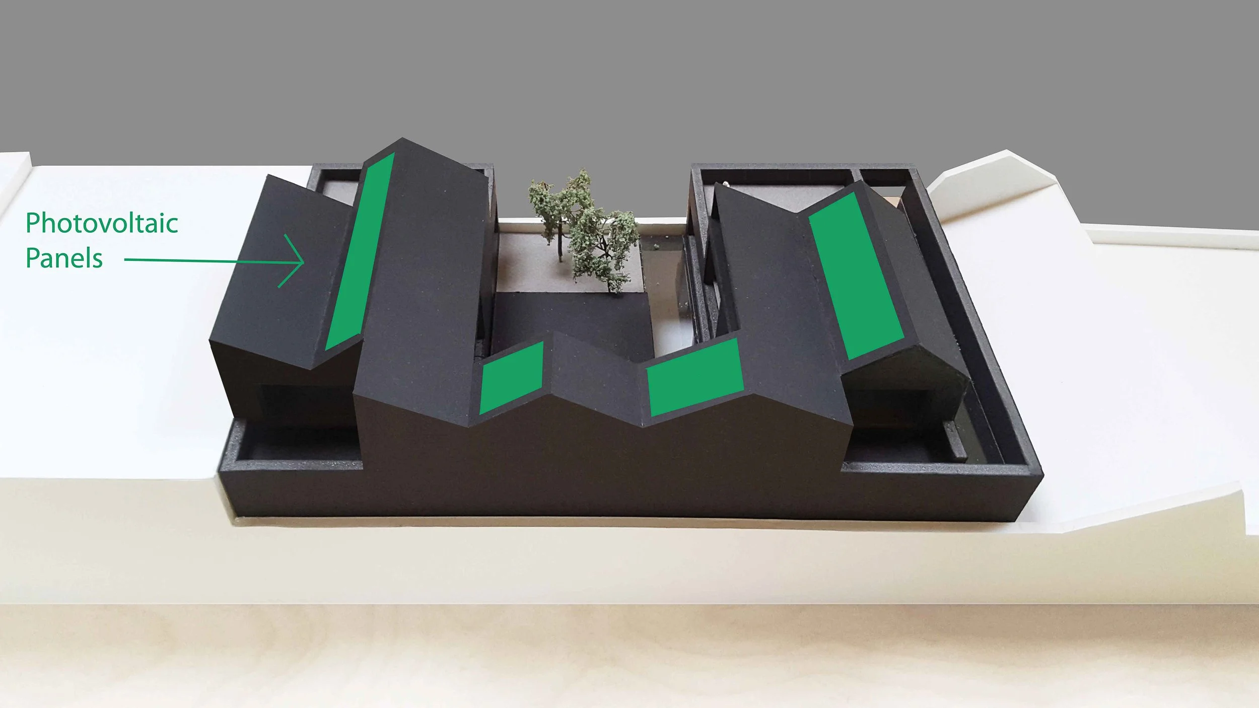 Architectural model of a modern building with black facades and green panels, surrounded by small trees.