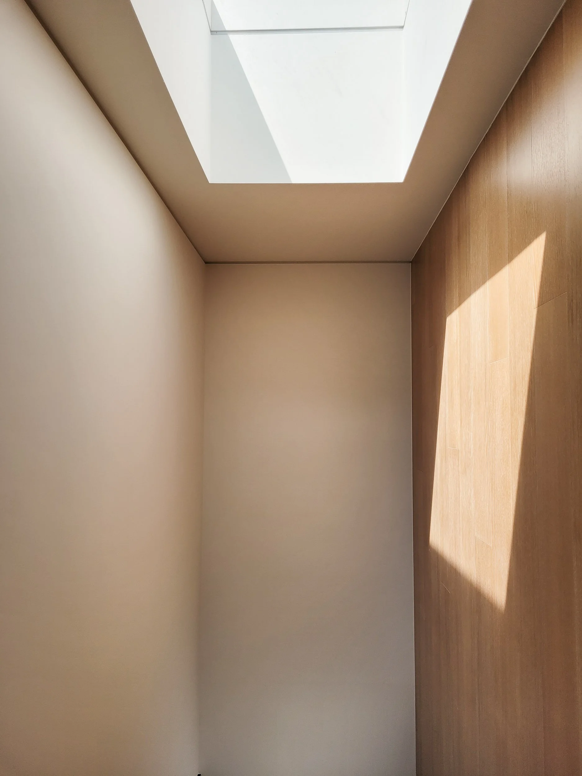 Empty room with beige walls, wooden flooring, and a skylight window on the ceiling.