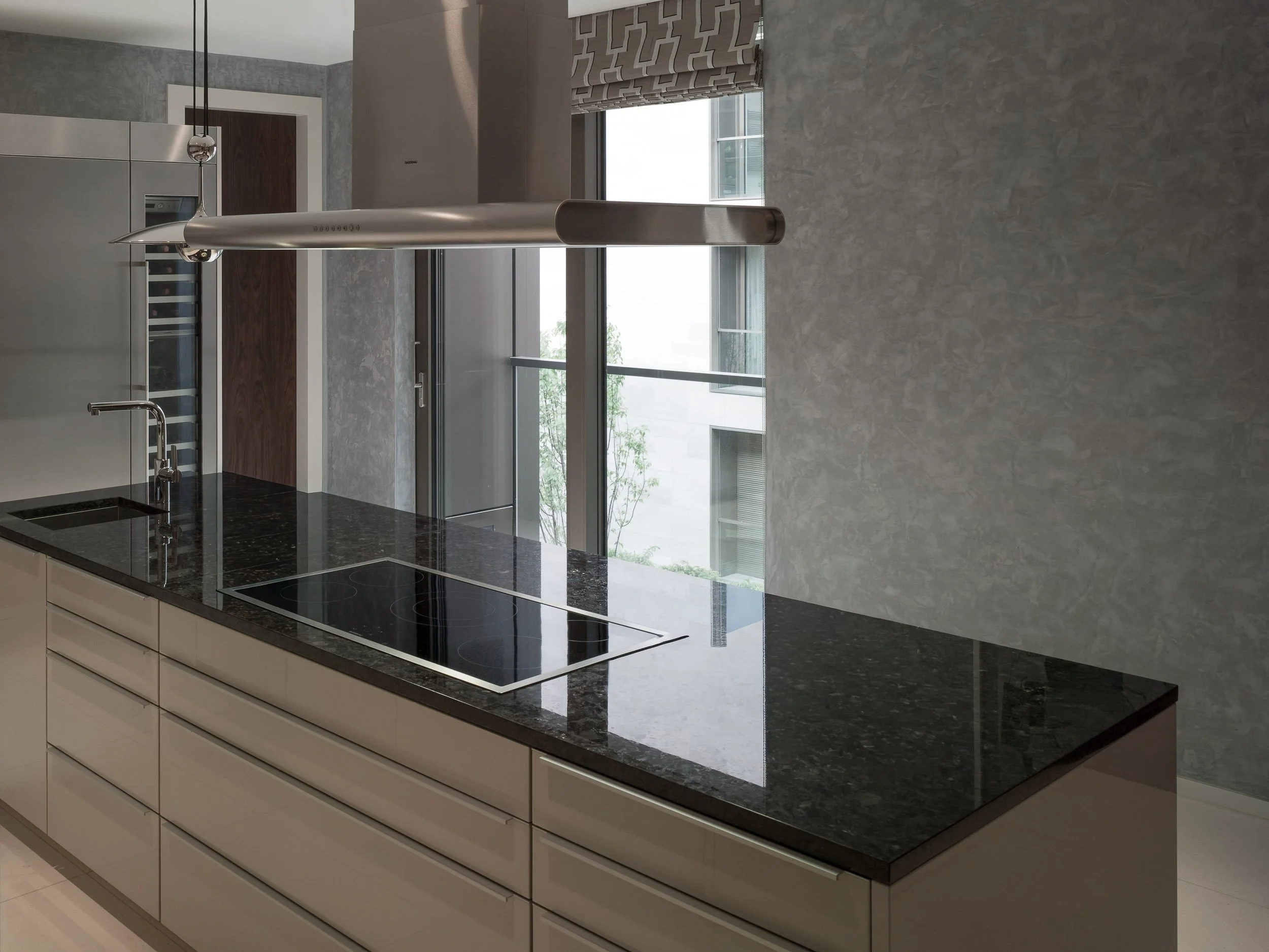 Modern kitchen with white cabinets, black granite countertop, stainless steel range hood, induction cooktop, and large windows with a view of trees outside.