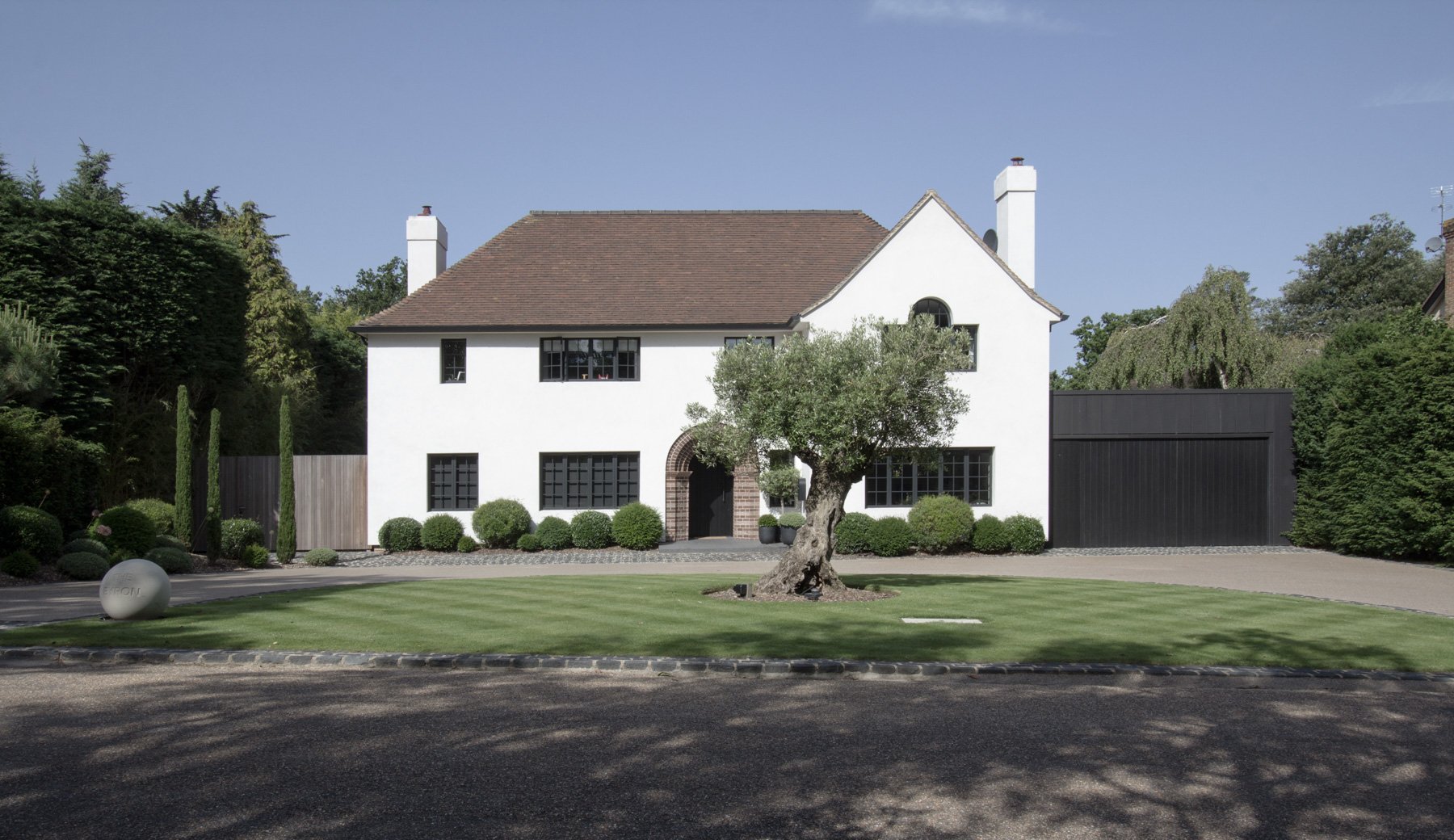 Front view of a white two-story house with a brown roof, surrounded by a neatly mowed lawn, bushes, and trees, with a driveway on the right side.
