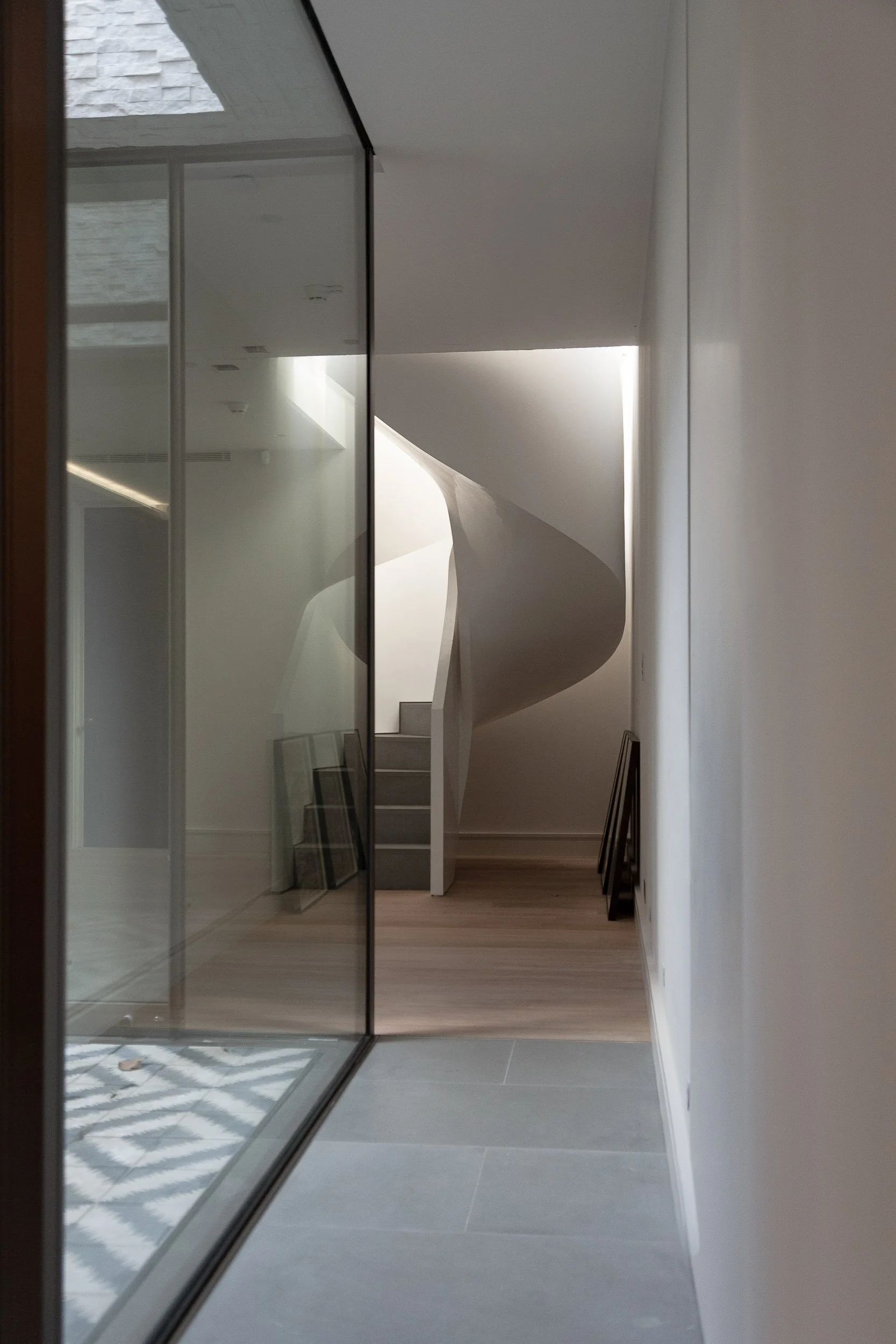 Modern interior hallway with glass wall, staircase, and wooden flooring, illuminated by natural light from a window.