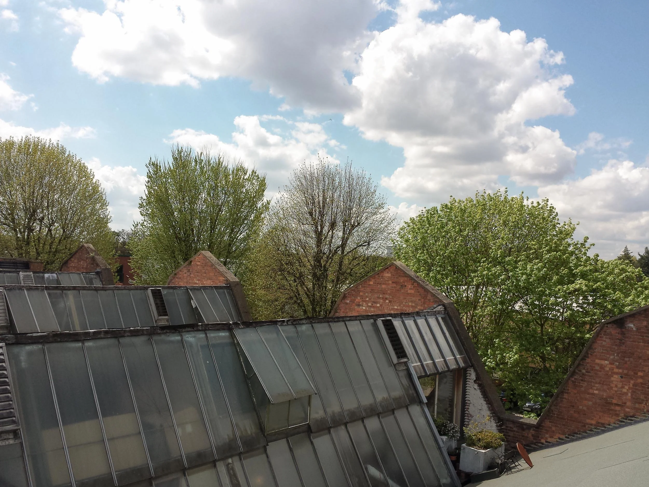 View of a cloudy sky above houses and trees, with part of a house roof in the foreground.