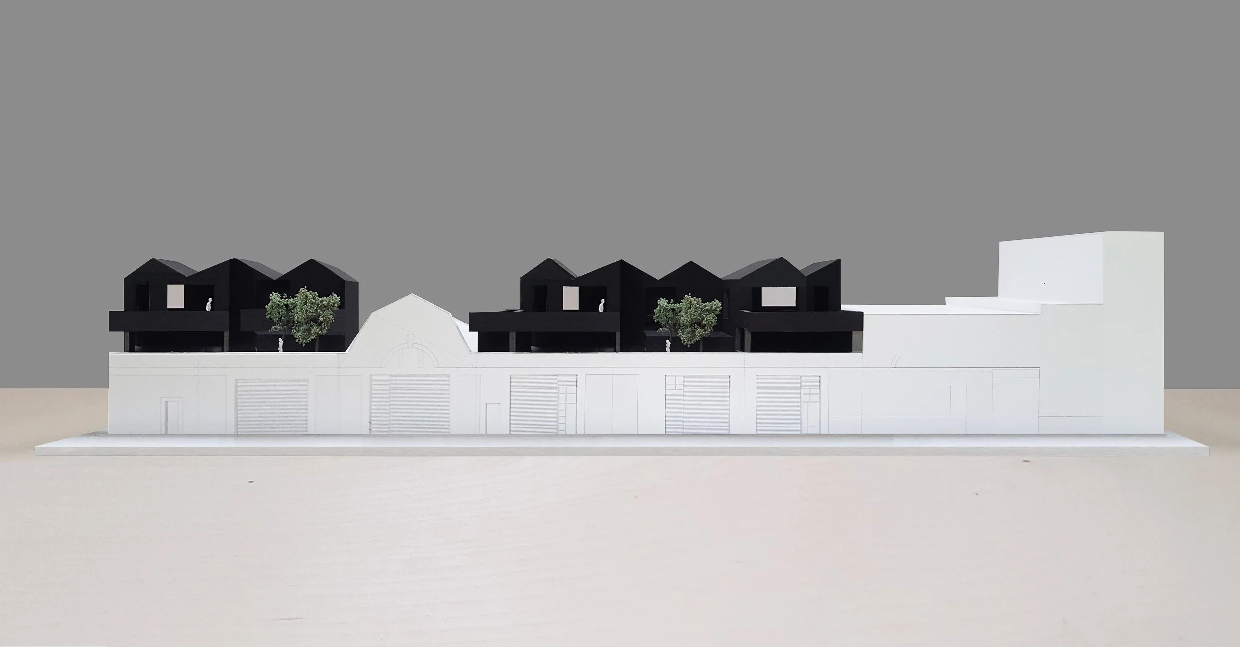 Architectural model of a modern, multi-story building with black upper structures, white lower base, and green trees, set against a plain grey background.