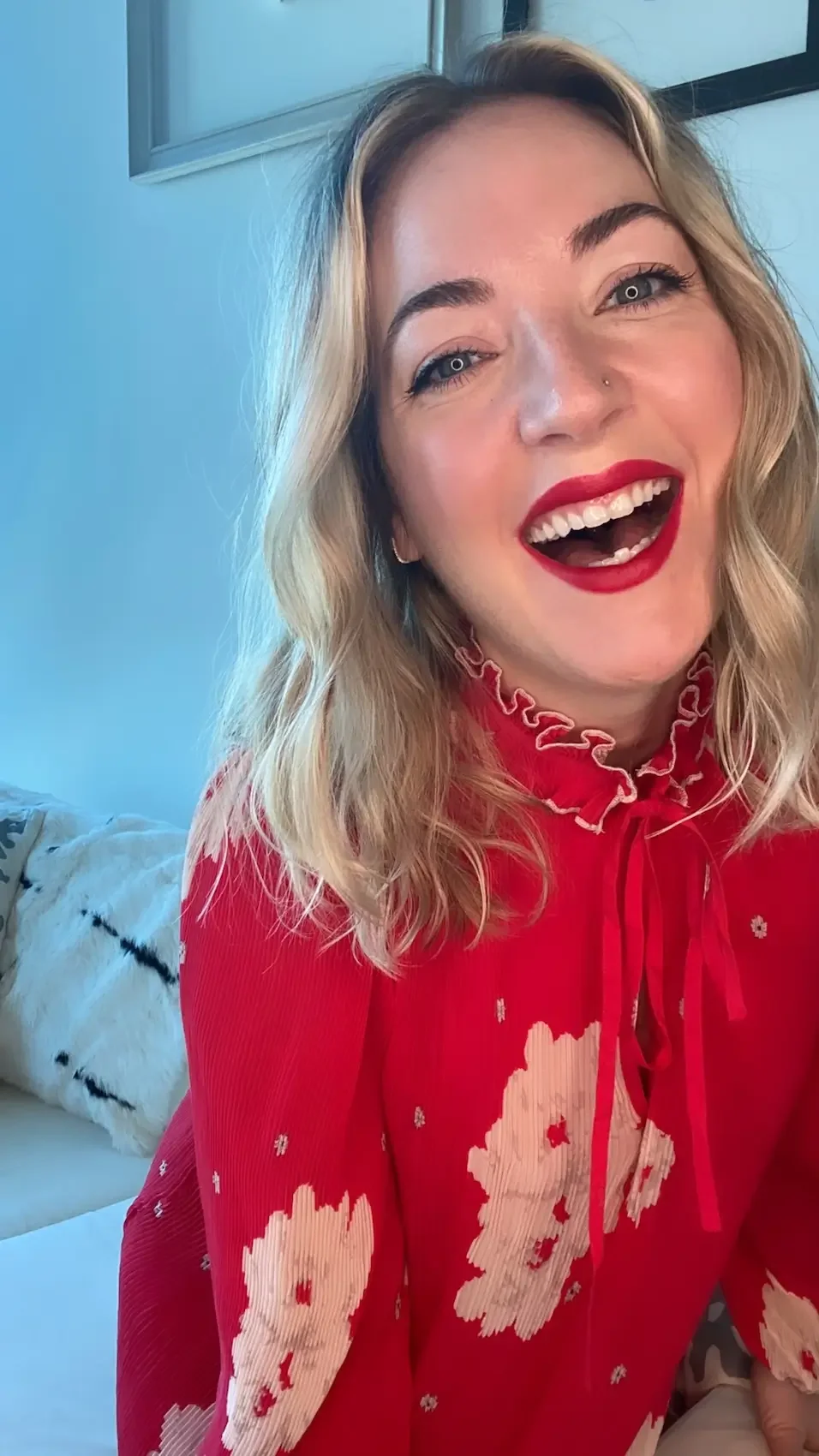 Nicole Russo, red lipstick, and a red dress with floral patterns, smiling and looking at the camera.