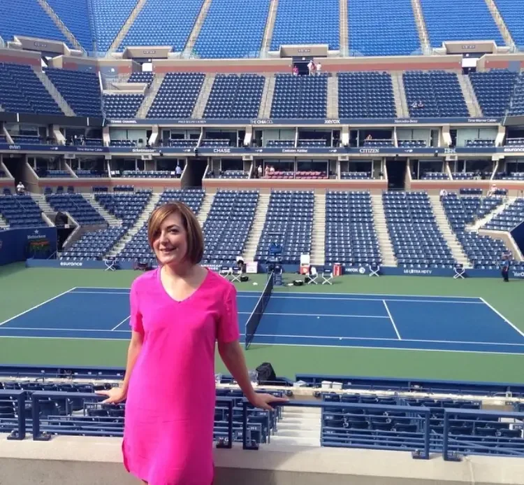 A woman in a pink dress standing in front of a tennis court inside a large stadium.