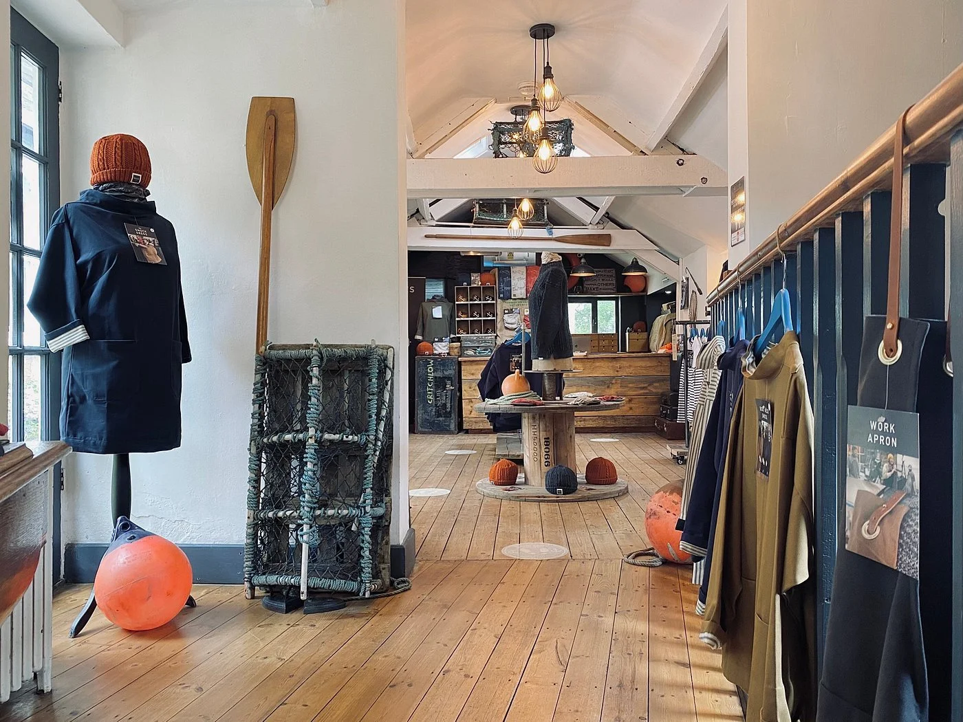 Interior of a retail store displaying jackets, hats, and accessories with wooden floors, model mannequin, and warm lighting.