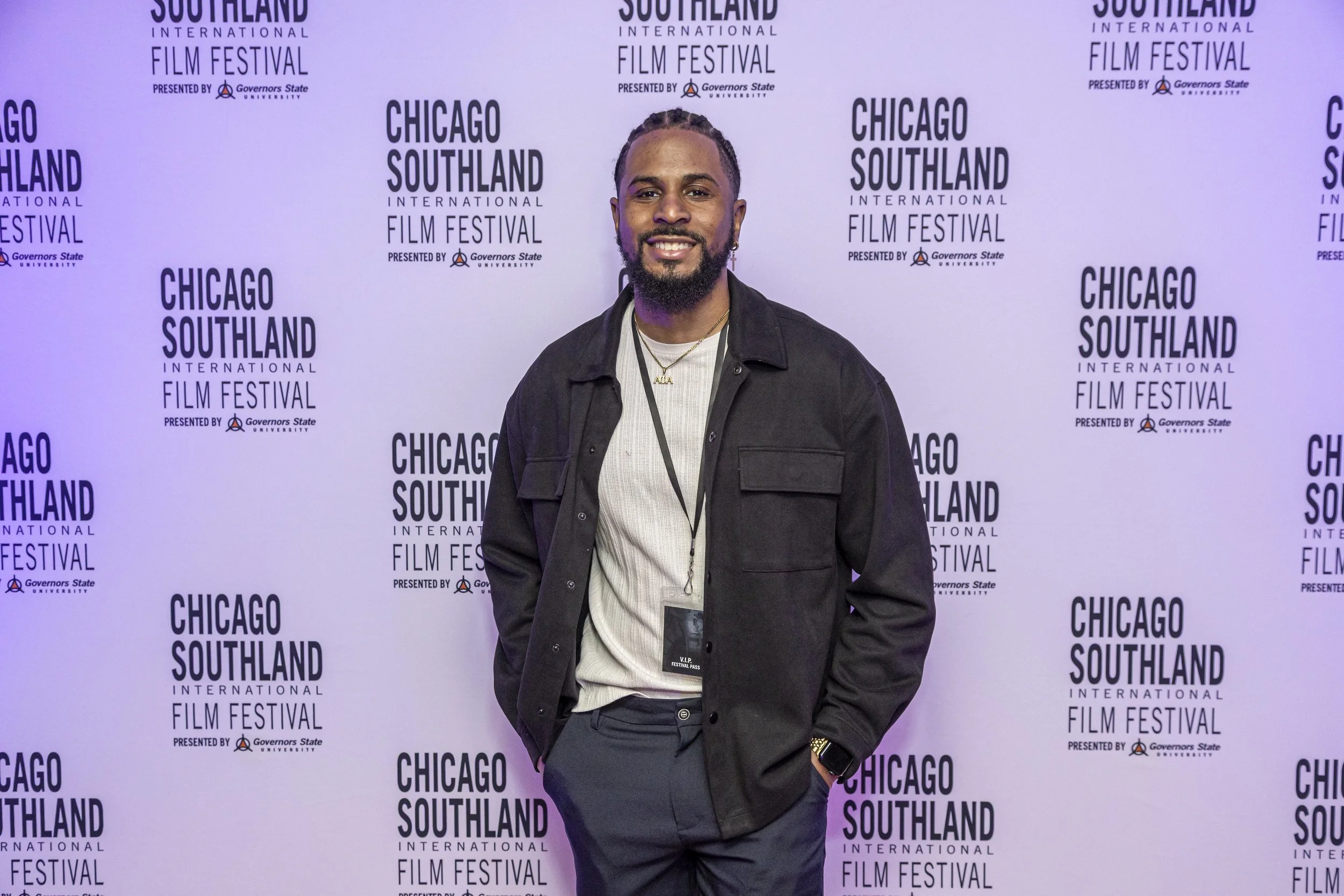 A man smiling at a film festival event standing in front of a step and repeat banner with 'Chicago Southland International Film Festival' printed repeatedly.