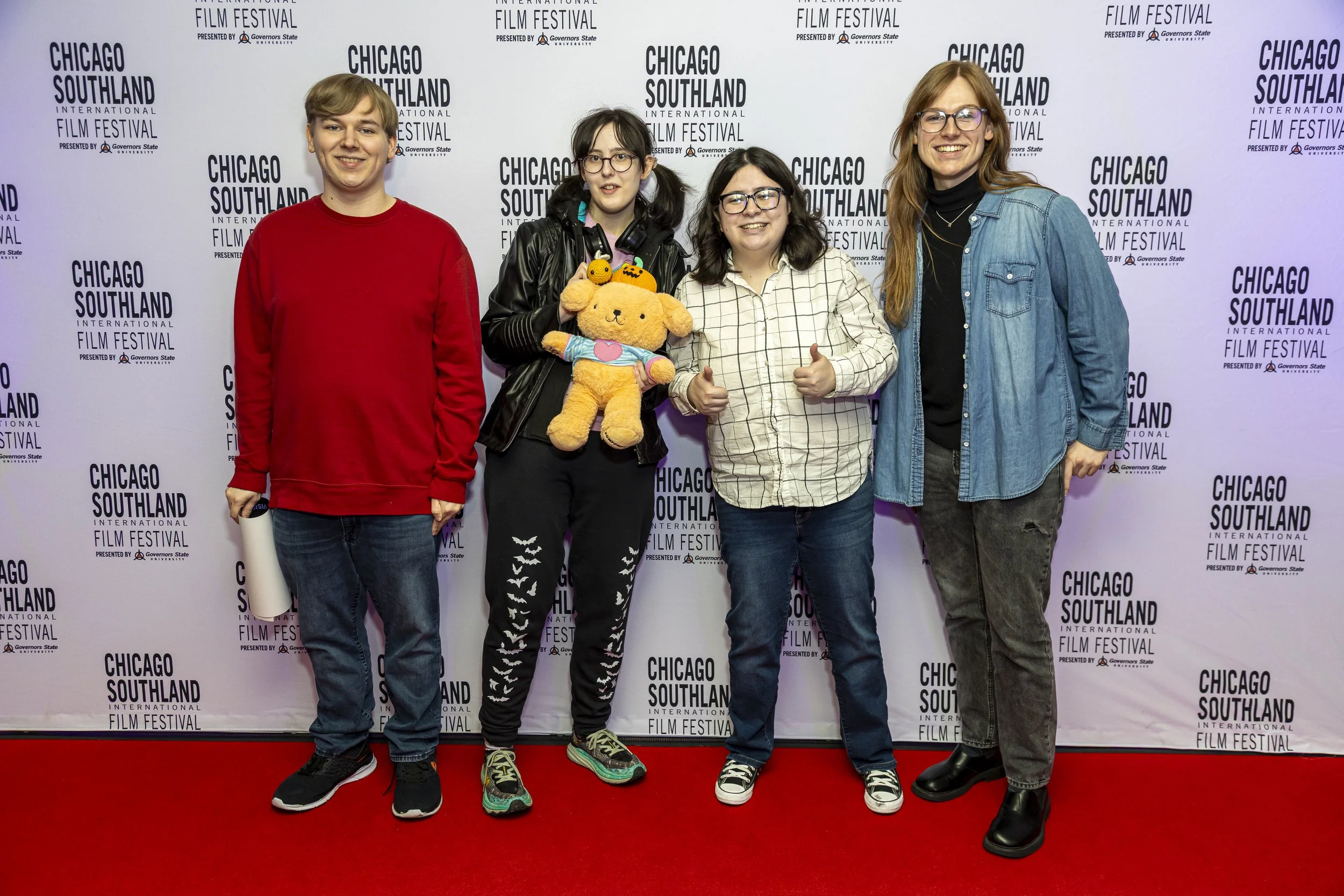 Group of four people smiling at the camera at the Chicago Southland International Film Festival, standing on a red carpet in front of a printed backdrop with the festival's logo.