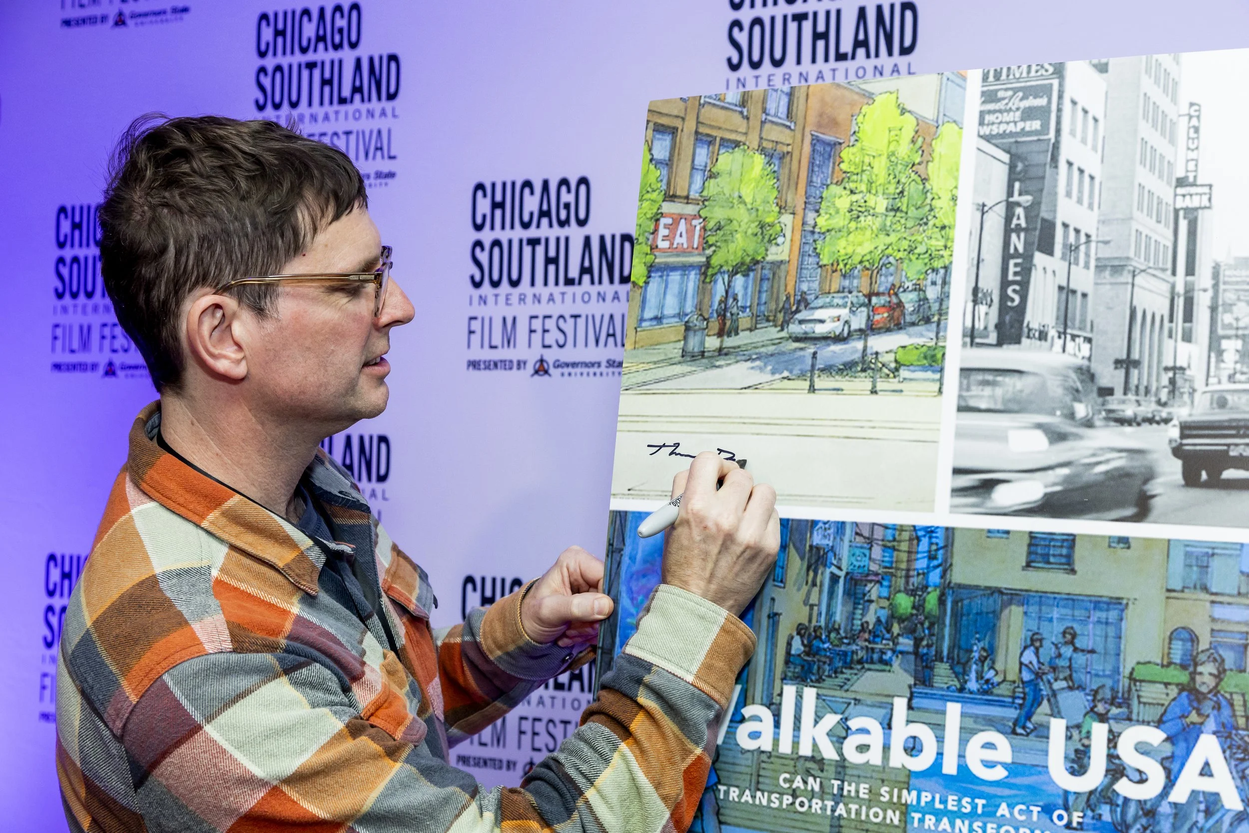 A man with glasses and a multicolored plaid shirt holding up a book or poster at the Chicago Southland International Film Festival.