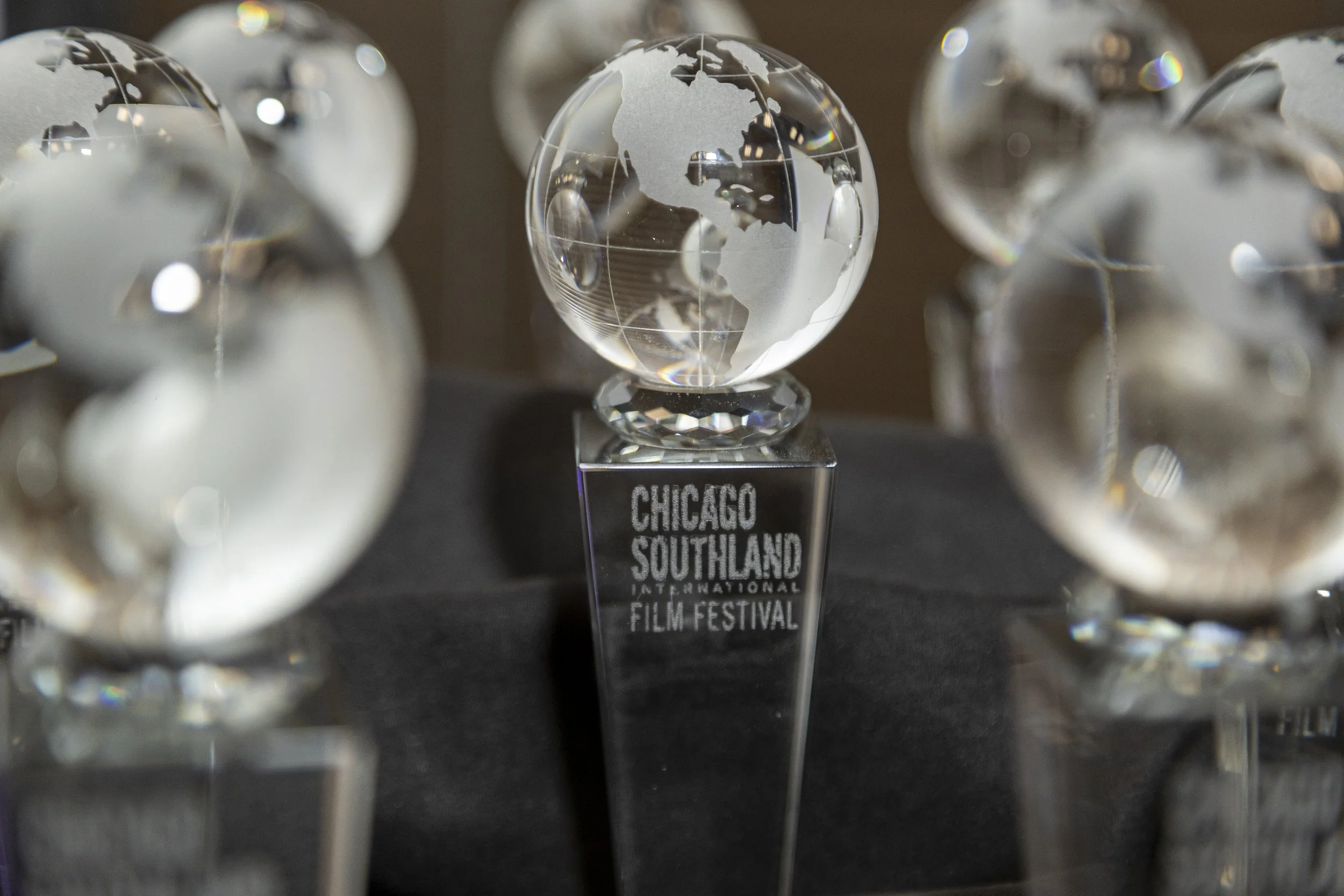 A crystal globe on a stand with a label reading 'Chicago Southland International Film Festival' in front of a background of multiple similar globes.