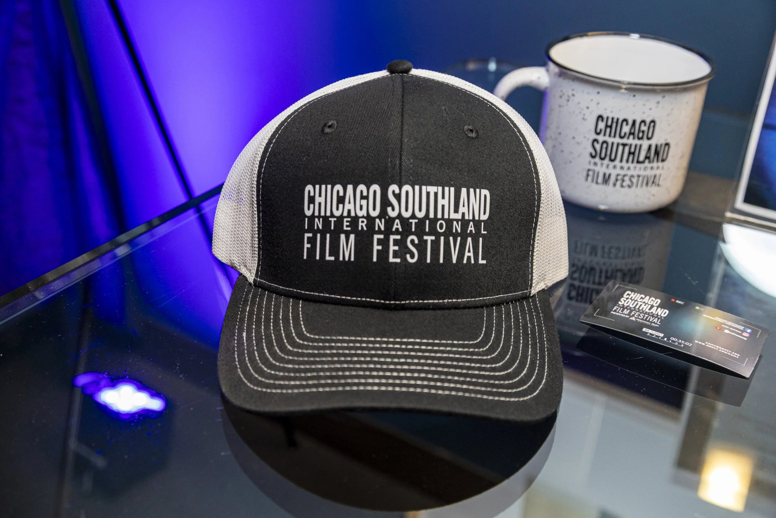 Black and white baseball cap with 'Chicago Southland International Film Festival' written on the front, placed on a reflective black surface.