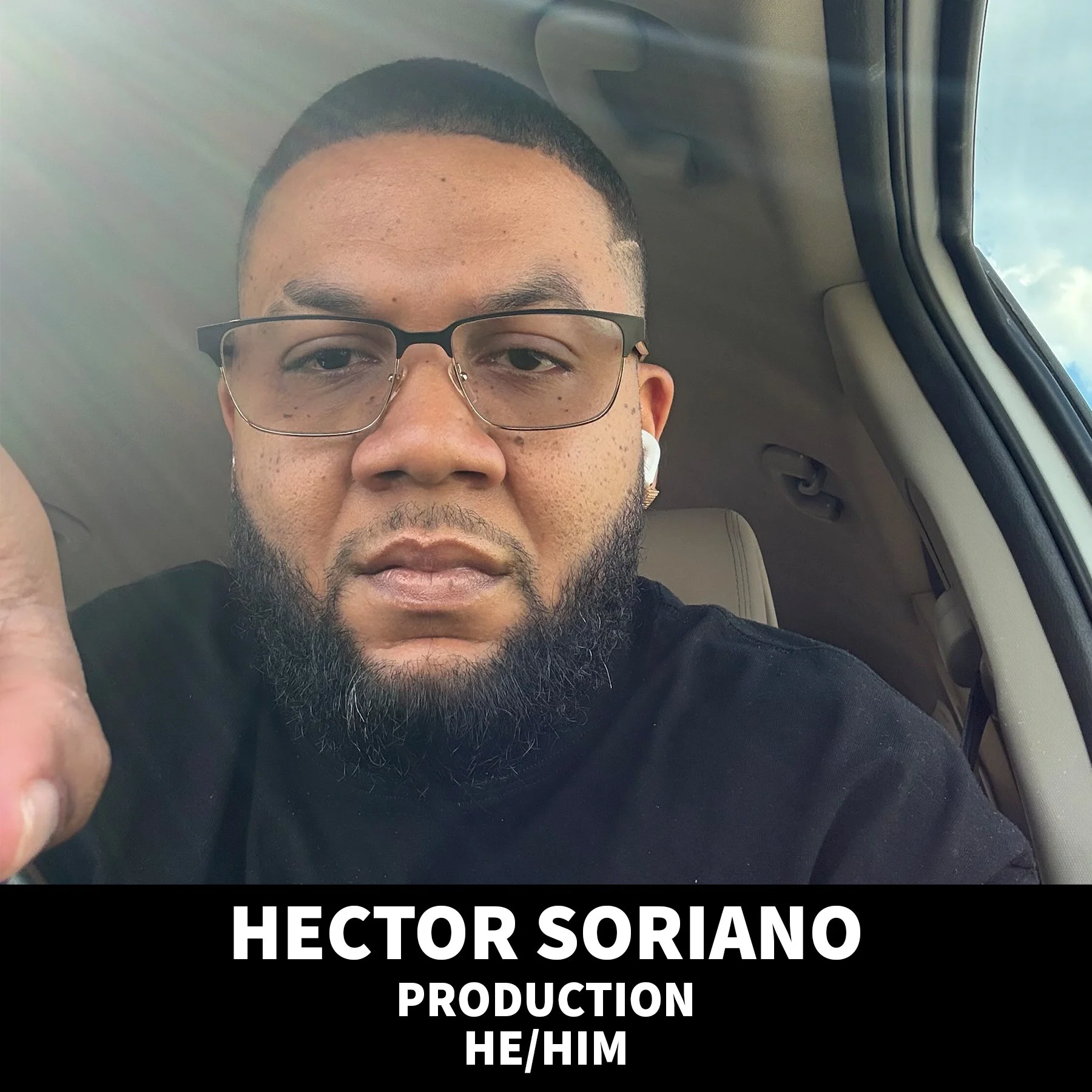 Portrait of a smiling man with a beard wearing a black baseball cap and black t-shirt against a black background.