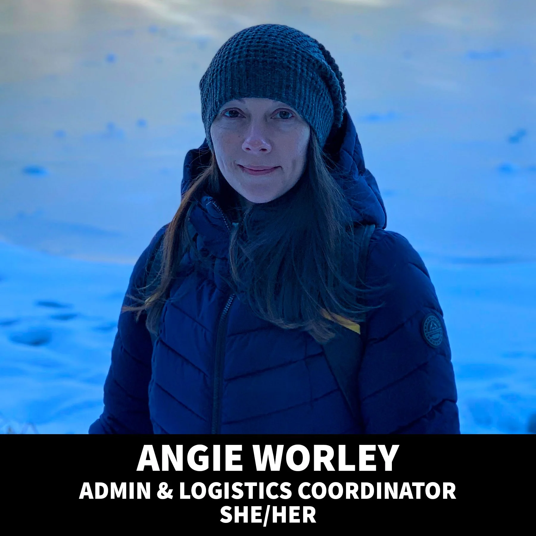 A woman with shoulder-length brown hair wearing a black top, smiling against a black background.