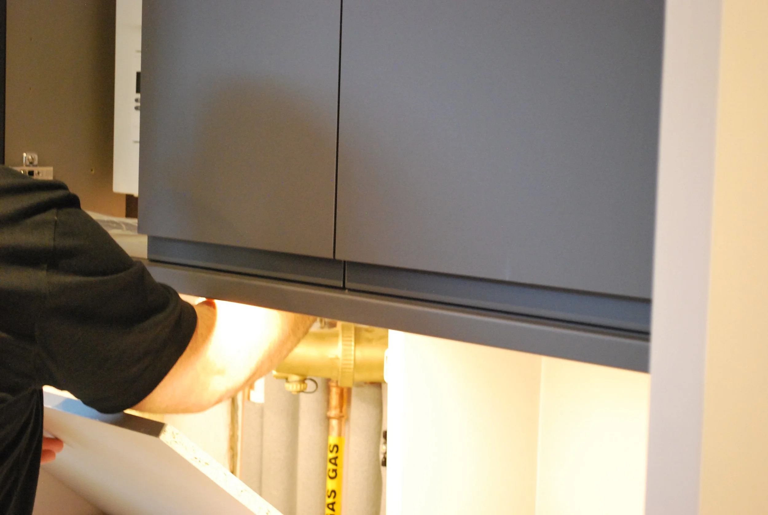 Service access beneath fitted cabinetry showing concealed gas and plumbing connections