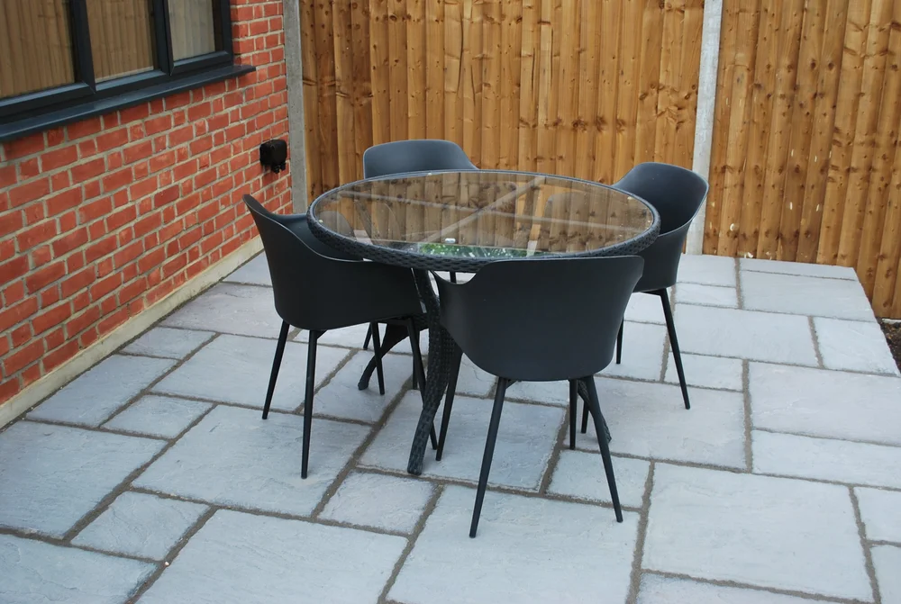Paved garden seating area beside a brick extension and timber boundary fence