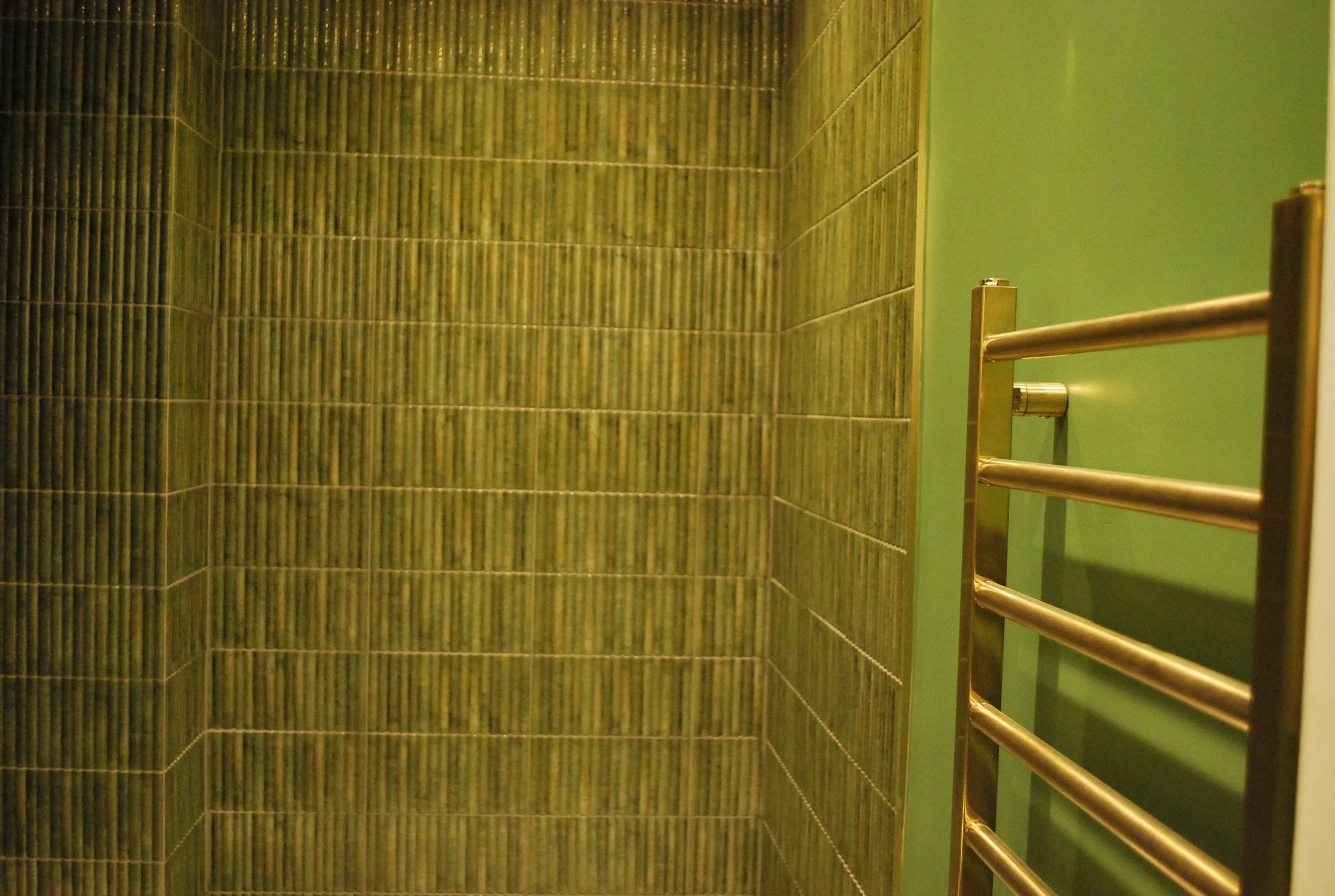 Walk-in shower tile detail beside a teal wall and chrome heated towel rail