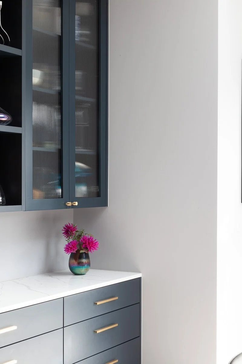 Detail of fitted kitchen cabinetry with ribbed-glass doors, dark frames and brass handles