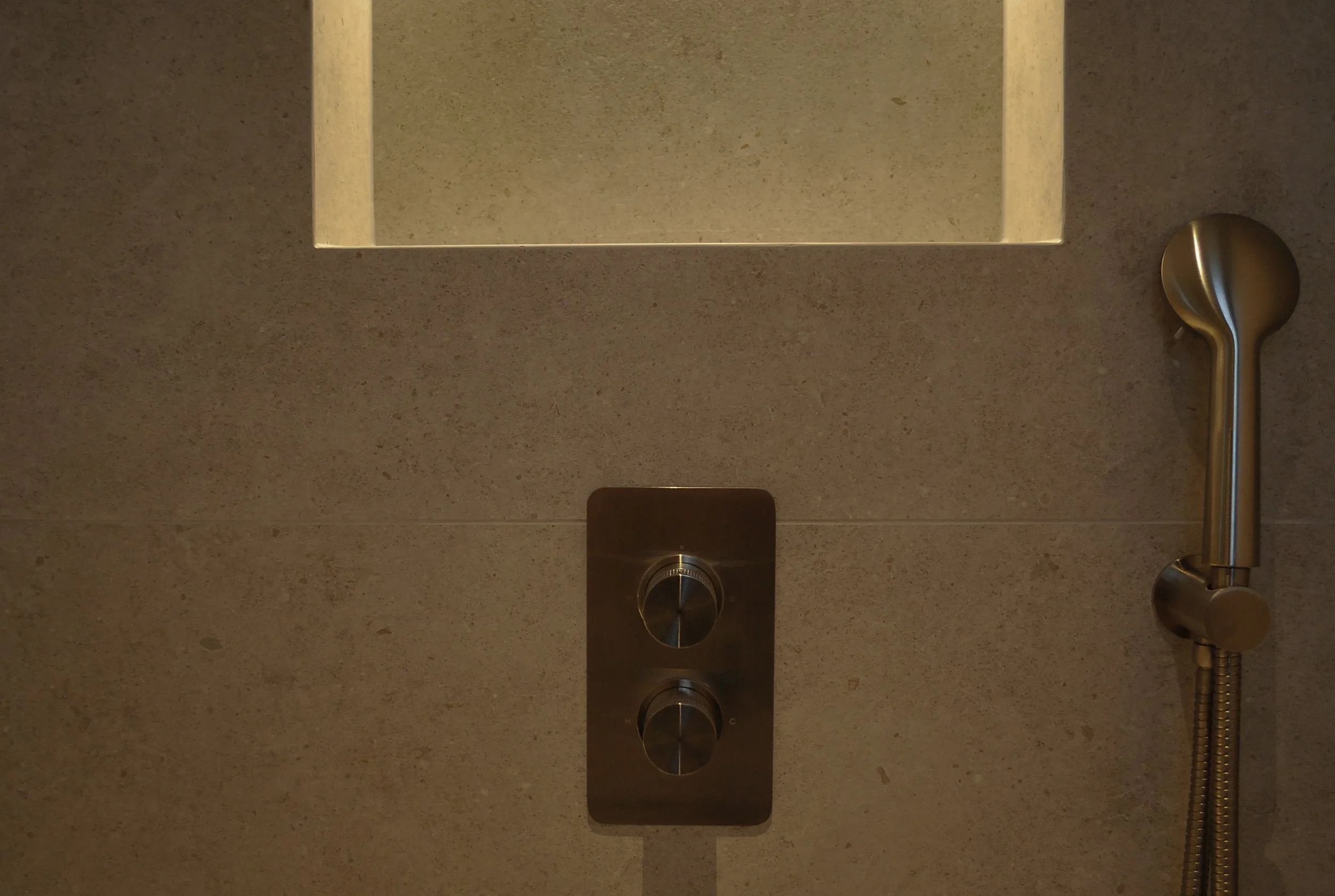 Concealed shower controls and hand shower fitted into a tiled bathroom wall