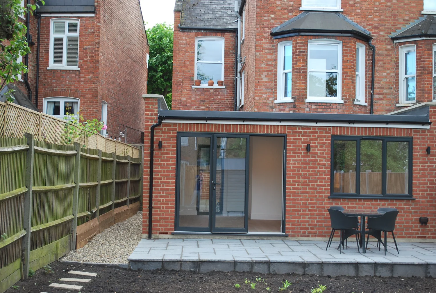 Rear of a London home with a paved patio, gravel side path, timber fencing and prepared planting areas