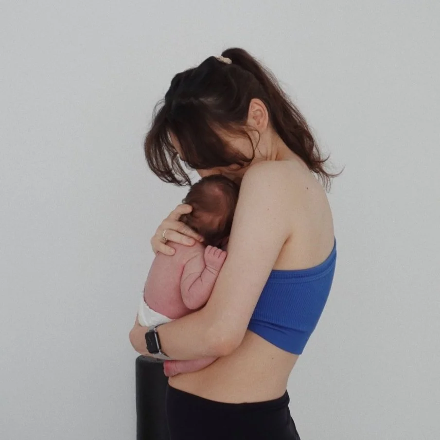 A woman cuddling a newborn baby wearing a blue top.