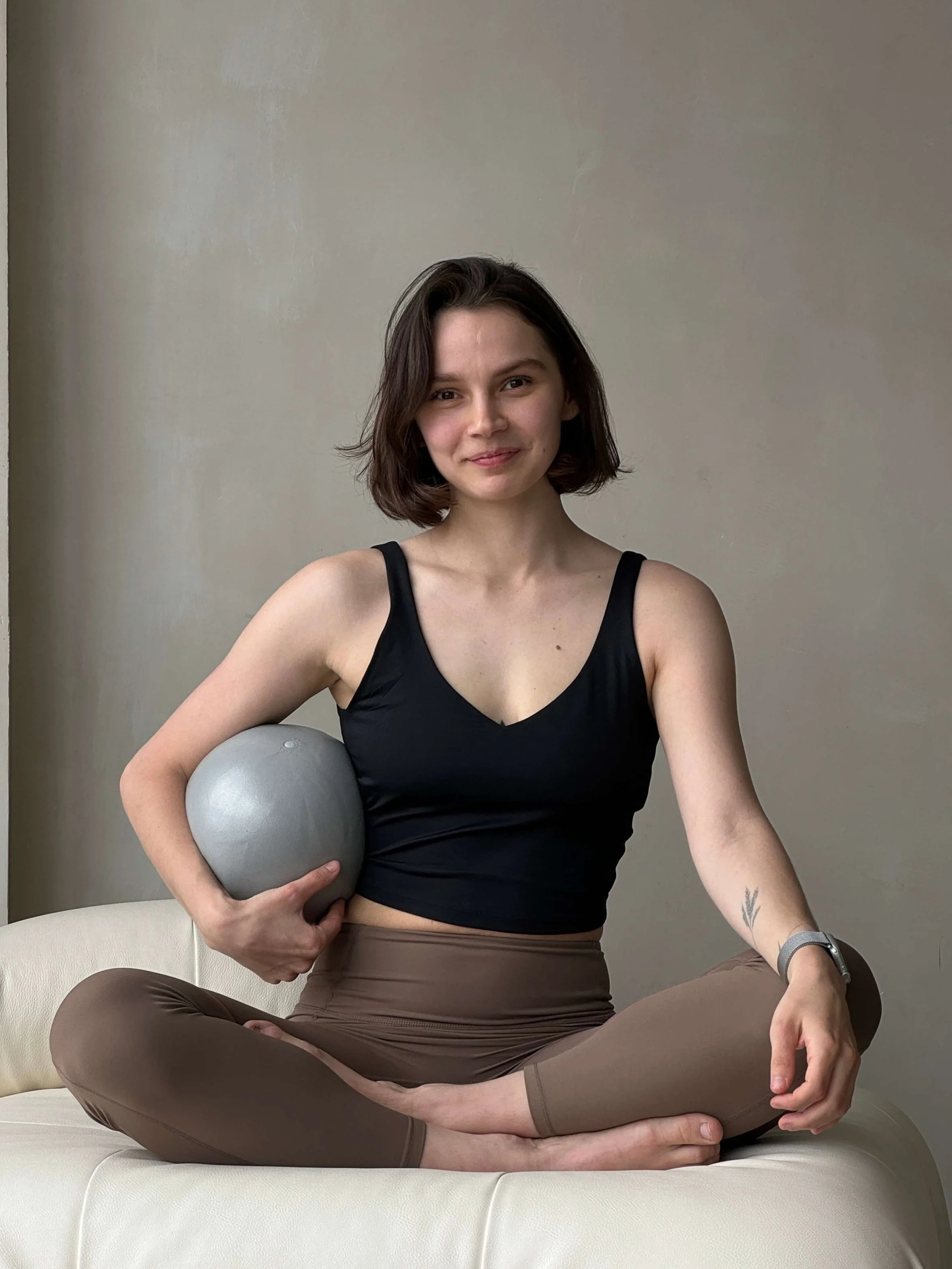 Person in athletic wear holding a yoga ball, seated cross-legged on a white couch.