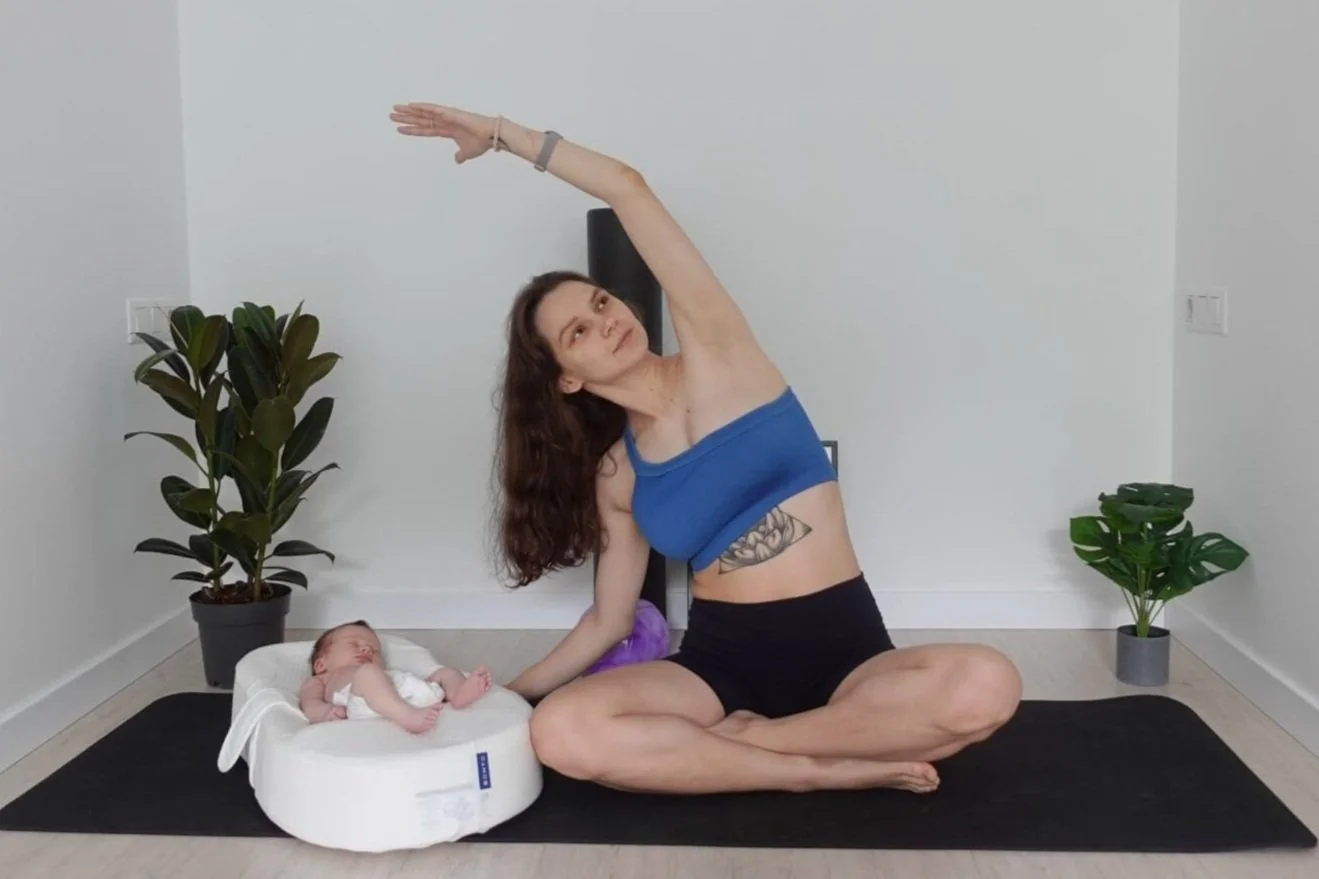 Woman doing yoga stretch on a mat beside a baby in a lounger, with two potted plants nearby.