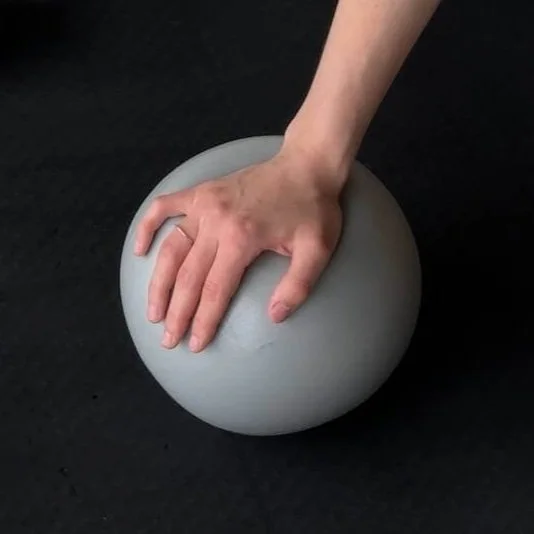 Hand pressing on a gray exercise ball on a black surface.