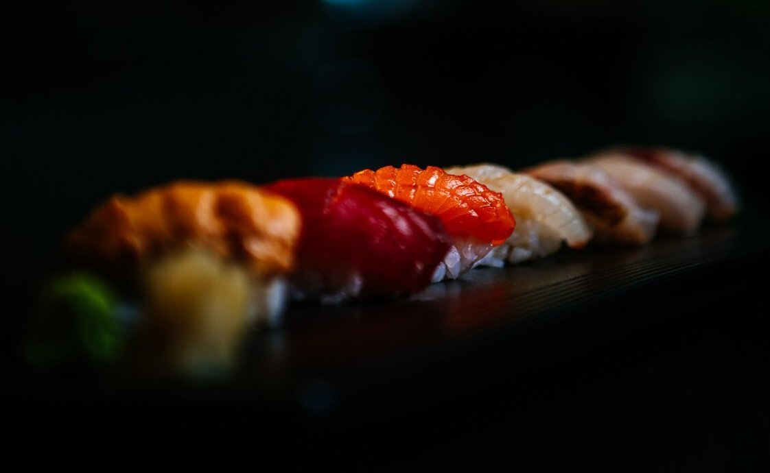 Close-up of assorted sushi pieces on a dark surface, with salmon, tuna, and other fish slices.