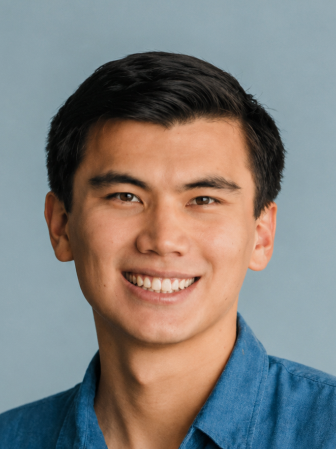 A young man with dark hair smiling, wearing a blue shirt, against a light blue background.