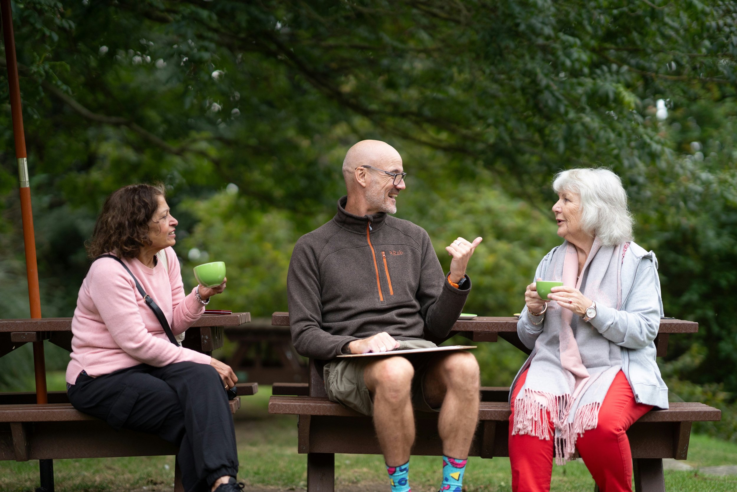 man and two women talking on a park bench