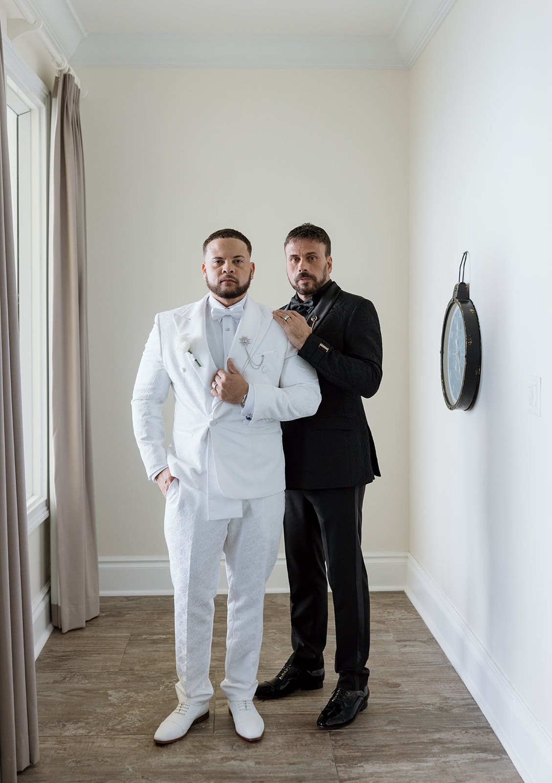 Two men standing indoors, one in a white suit and the other in a black suit, posing for a photo.